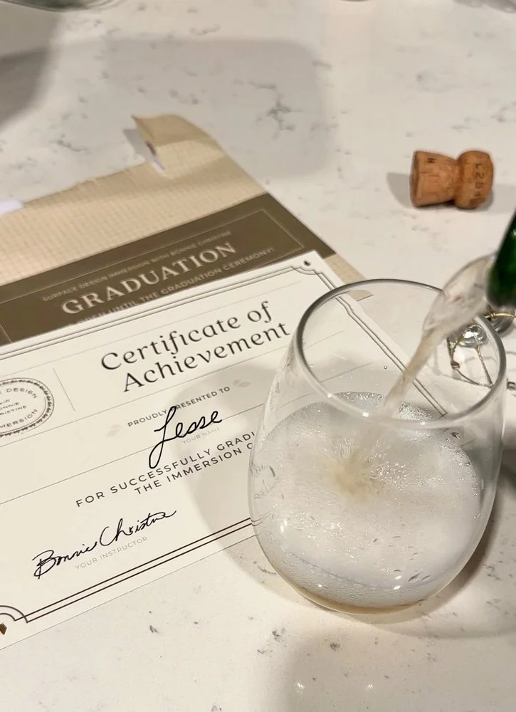 Overhead shot of someone pouring champagne next to a graduation certificate for Immersion 2026.