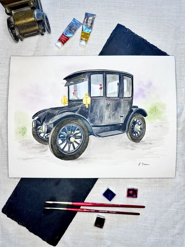 Watercolor painting of a vintage black car with lanterns on the front, placed on a table with painting supplies including brushes, paint jars, black cloth, and a piece of dark fabric.