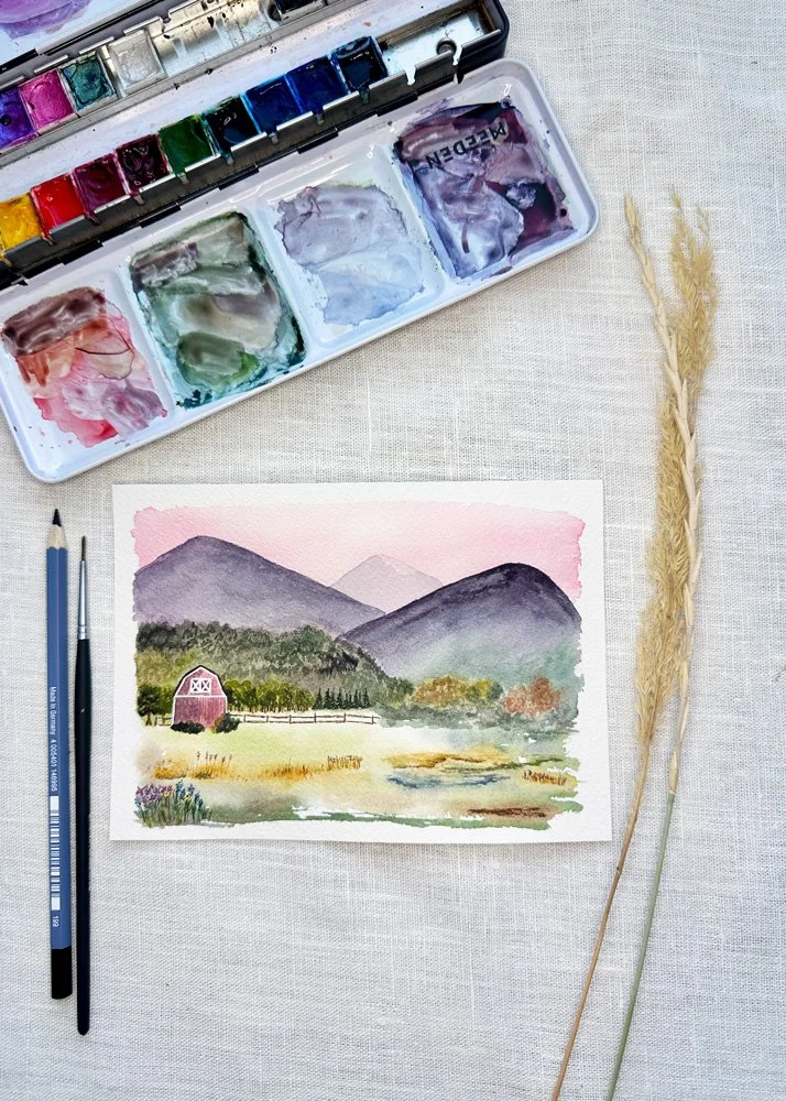 overhead view of a fall watercolor painting featuring a barn and mountains