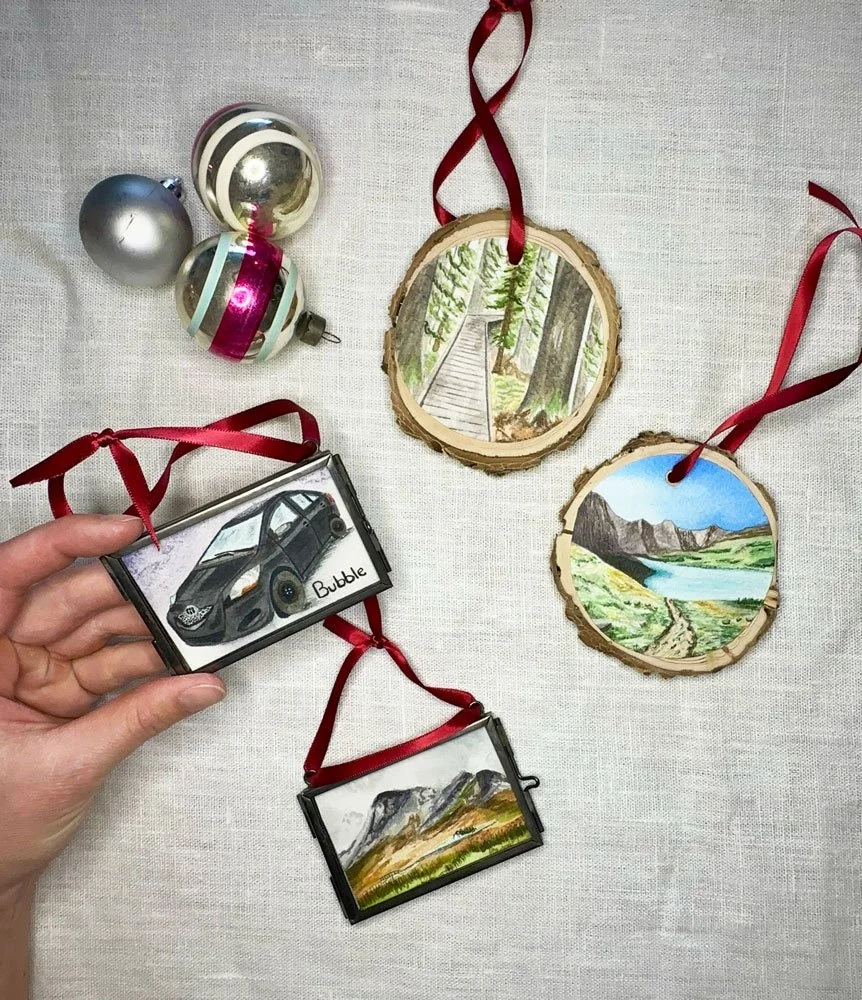 flat lay of four holiday ornaments two painted on wooden rounds two in glass ornament frames