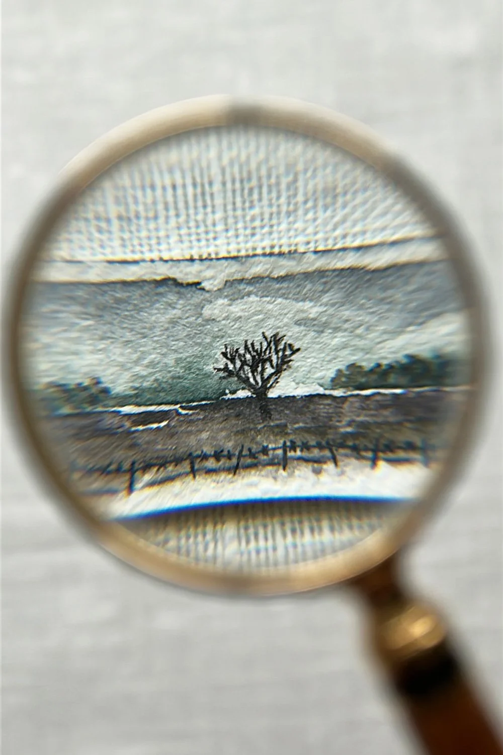 A magnifying glass focusing on a landscape painting featuring a solitary tree, hills, and a fence, with a cloudy sky in the background.
