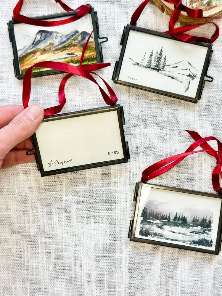 two watercolor ornaments in glass frames one showing the front and one showing the back