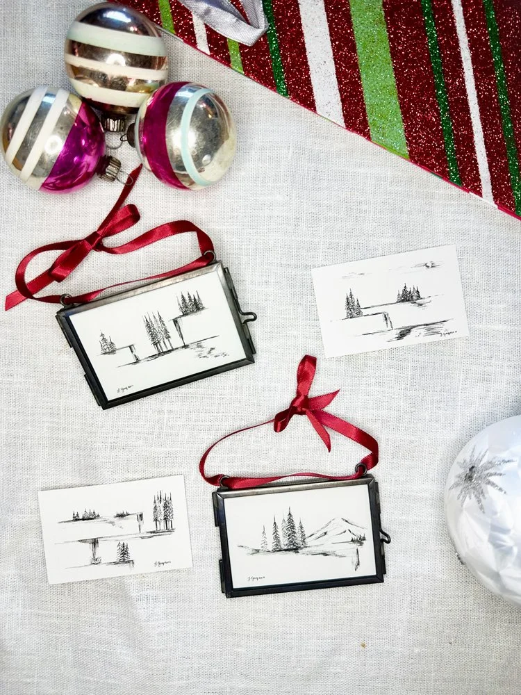 over head view of a holiday product scene featuring two pen drawings in glass ornament frames