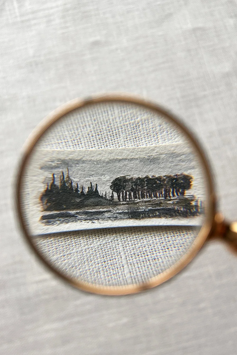 A small ink drawing of a landscape with trees and water, viewed through a magnifying glass.