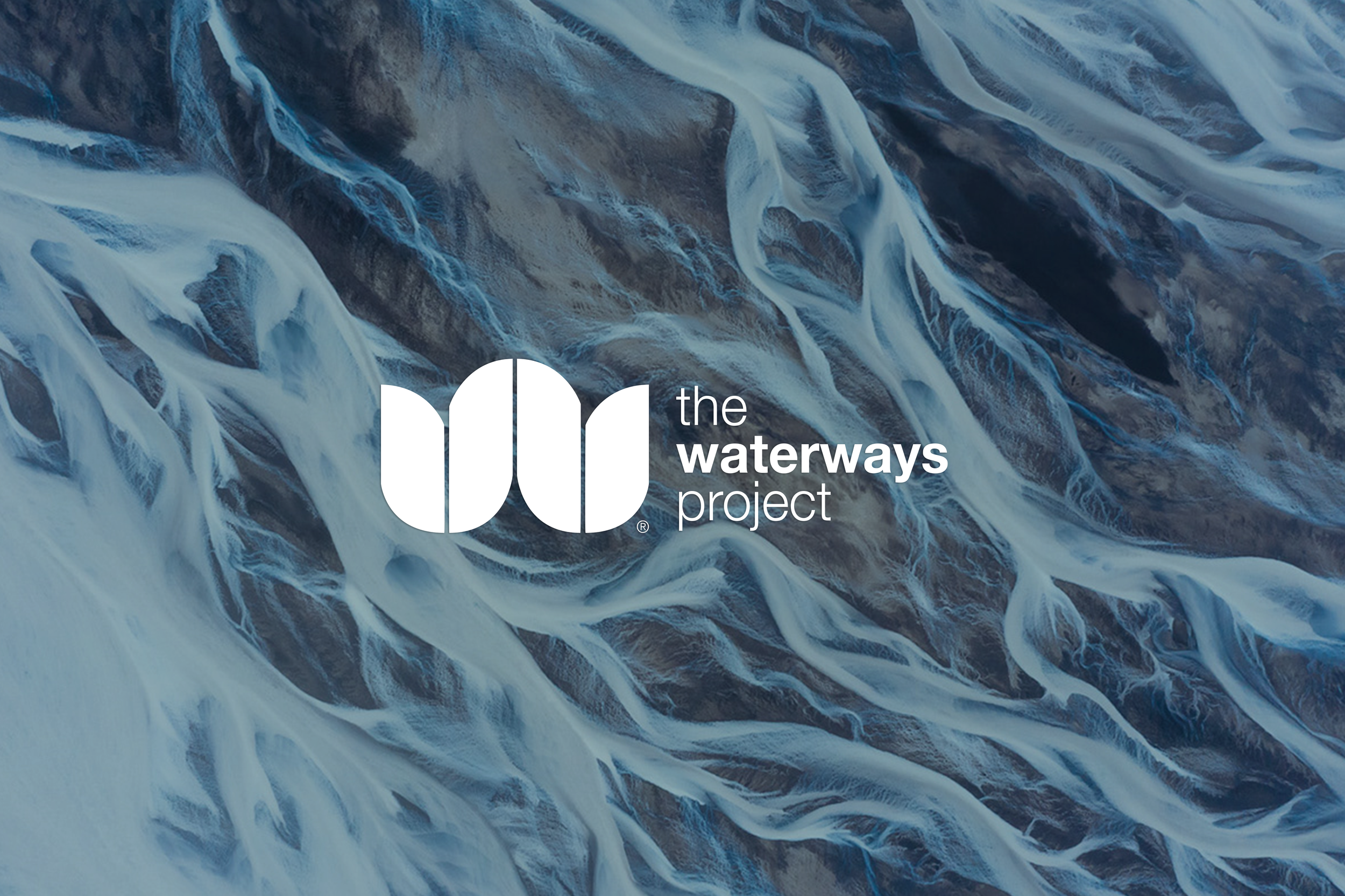 Aerial view of a river flowing through a landscape with brown terrain, showing white water and twists in the waterway. Overlay text reads 'the waterway project' with a stylized icon representing water.