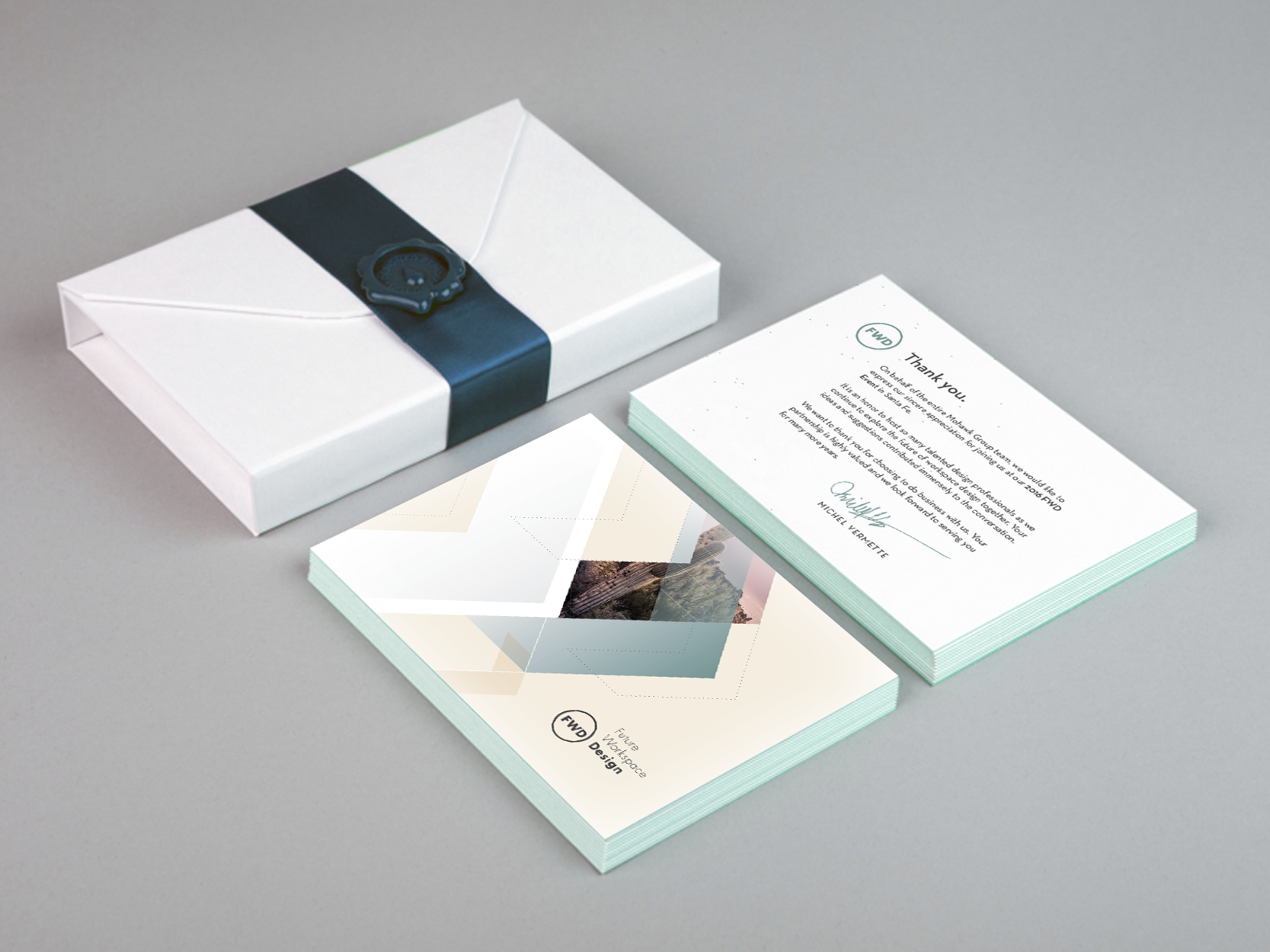 A white rectangular gift box with a black ribbon and a wax seal, a stack of thank you notes, and a designer brochure from Future Workspace Design, all placed on a gray surface.