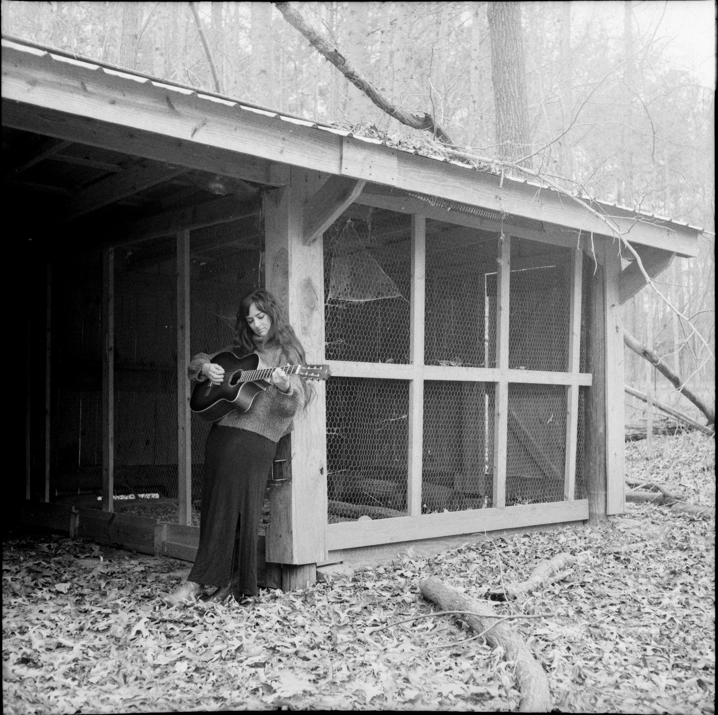 anna leaning on abandoned shed playing guitar on a cold winter day