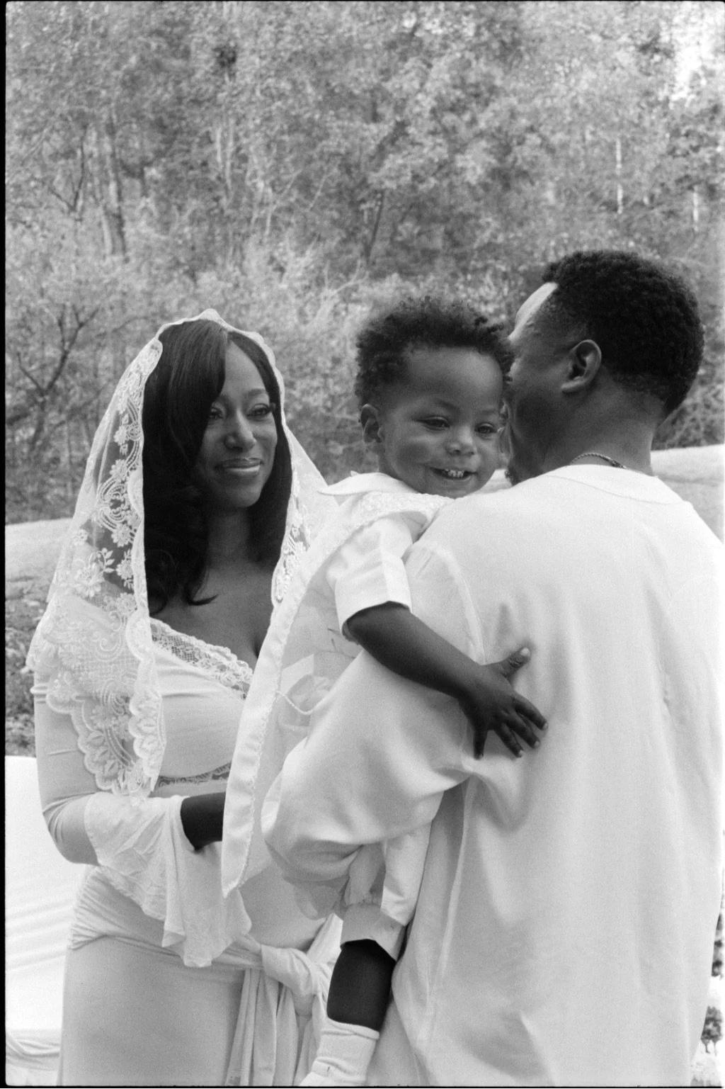 mom and dad holding their son during his baptism on b&w film