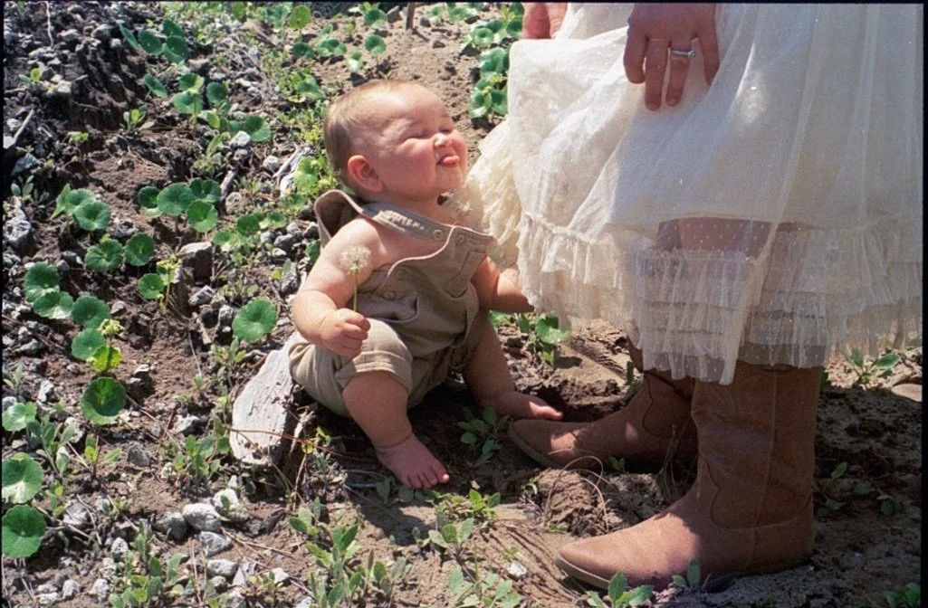 baby holding dandelion flower sitting in the grass smiling