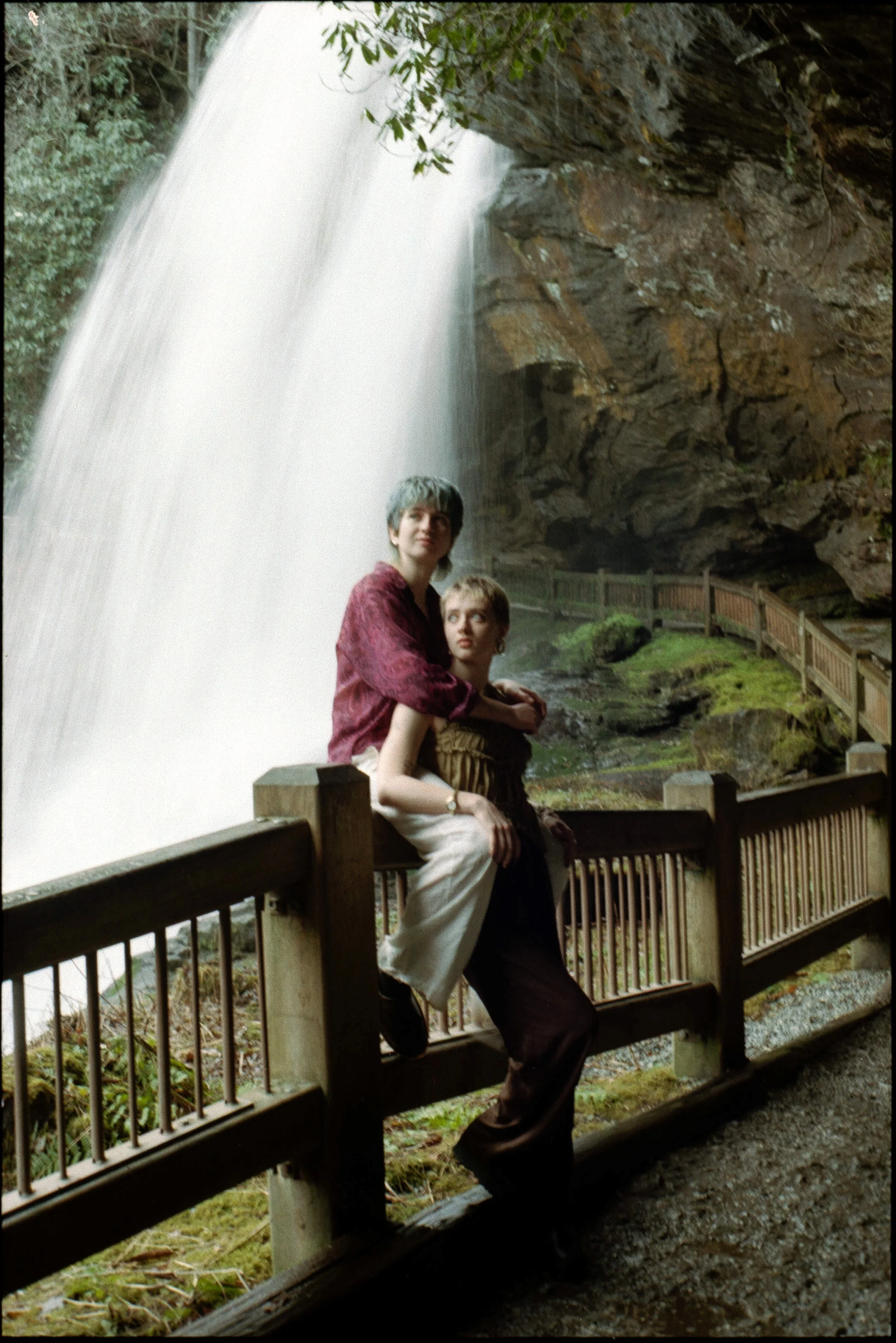 queer couple posing in front of waterfall in a fern gully inspired engagement session in north carolina on film