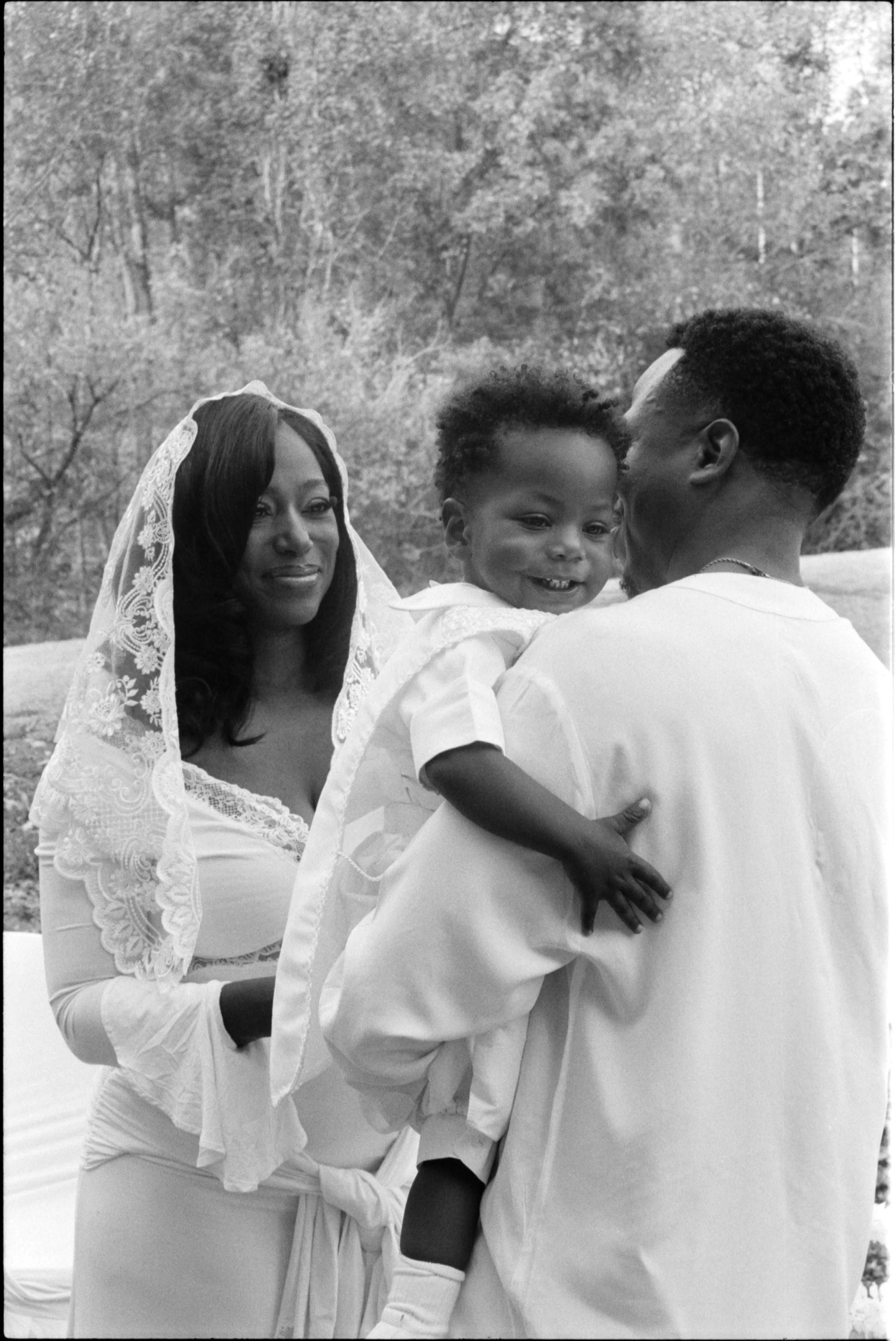 parents and son on his baptism captured on black and white film at a park in north carolina