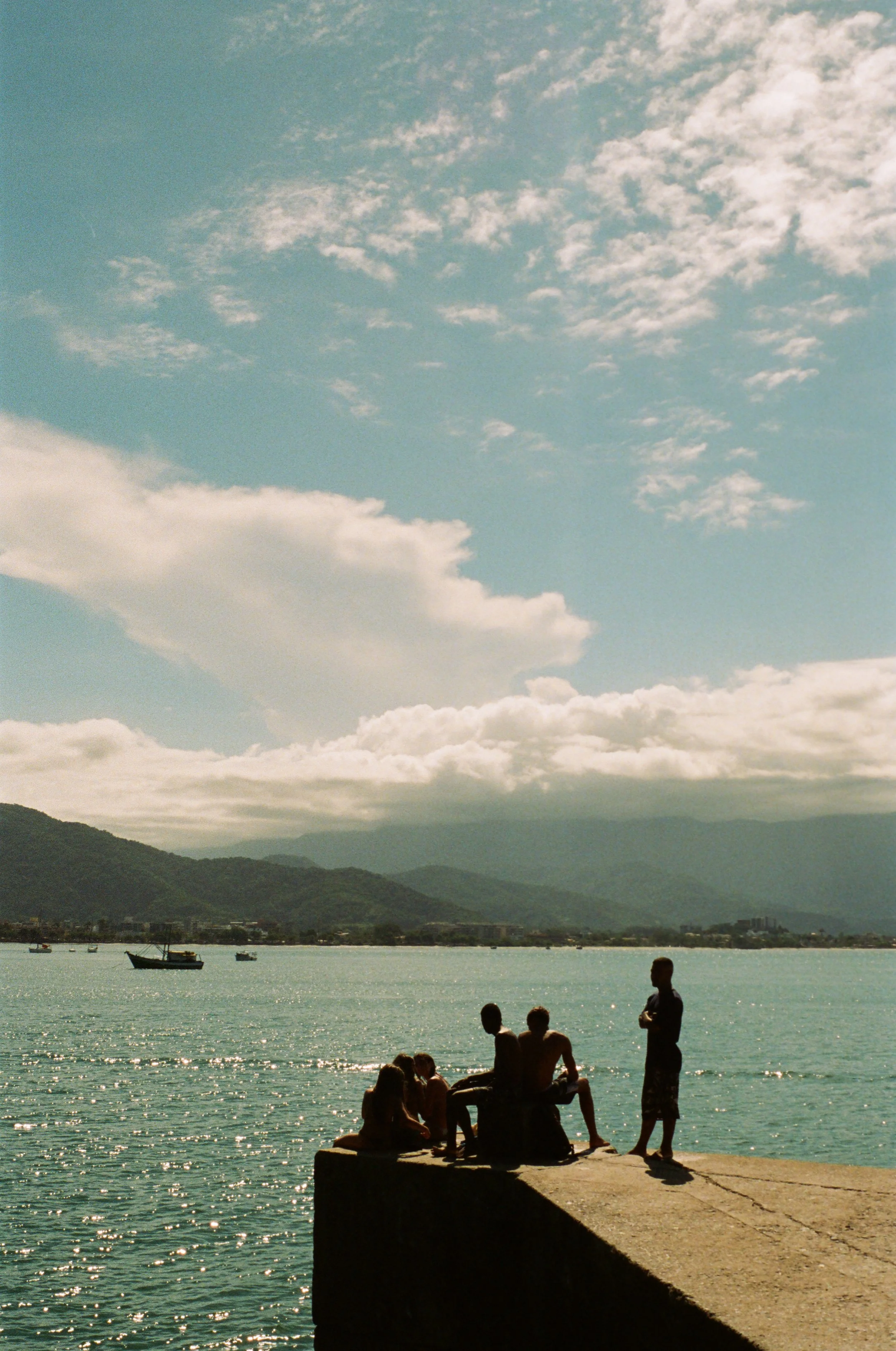 silhouette of brasil boys standing on the fishing pier with blue water