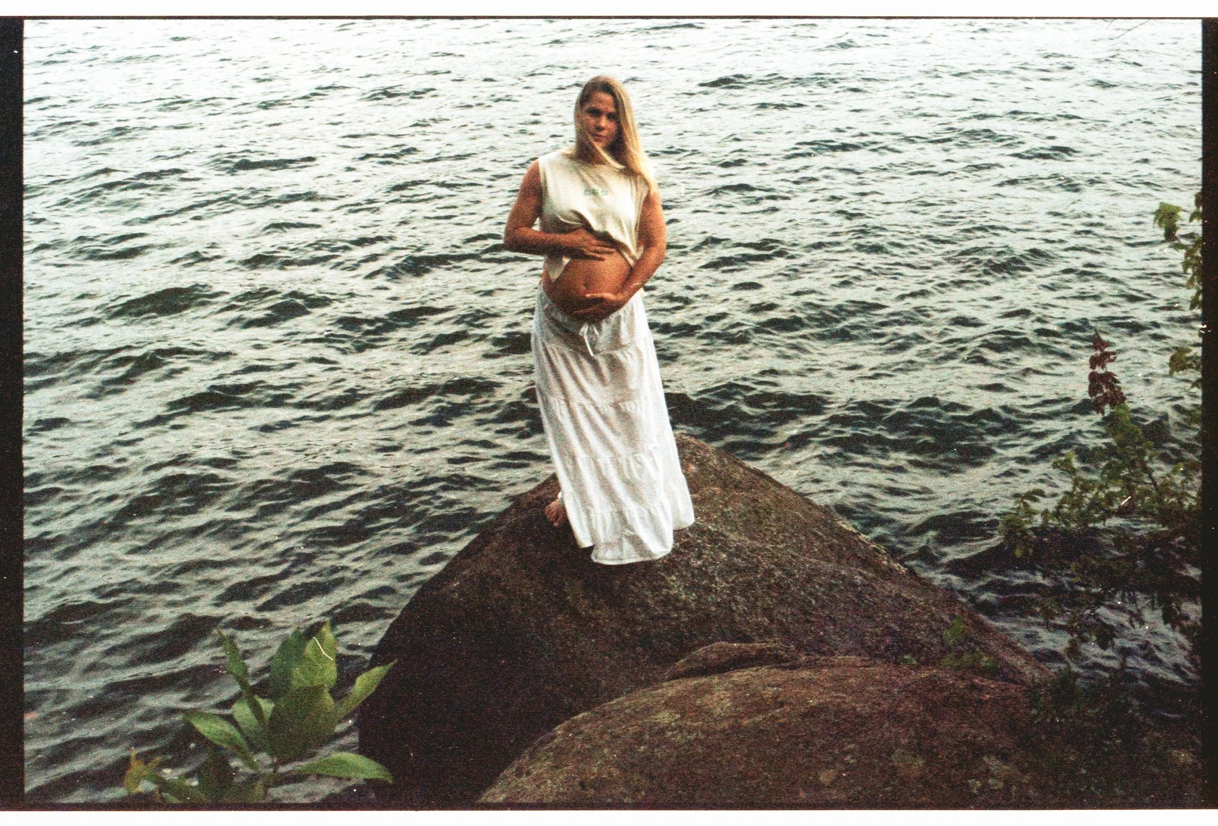 pregnant mama standing in the middle of the river holding her belly on film