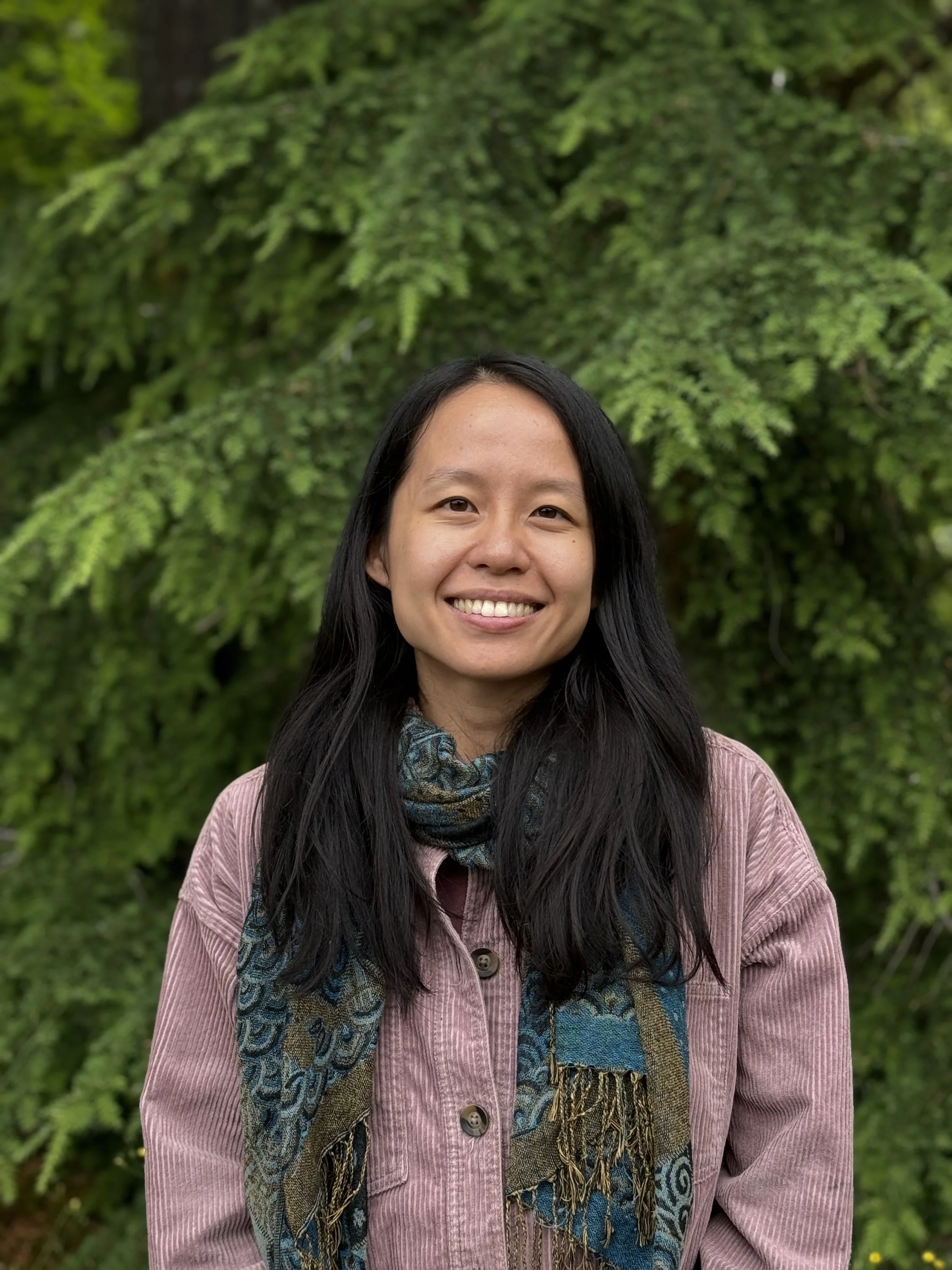 liz zhou, therapist in colorado, smiling in front of pine trees