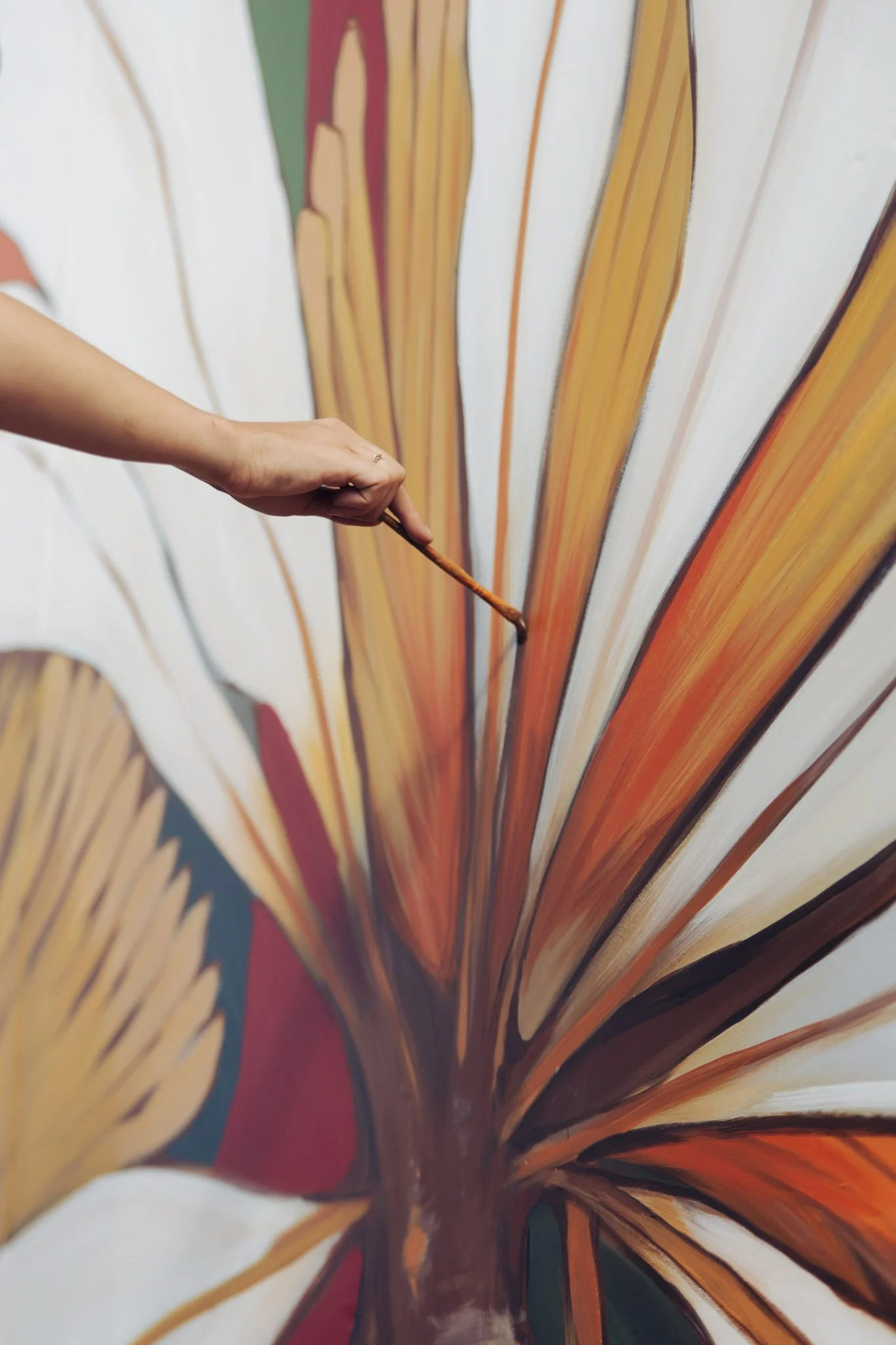 Person painting a large, colorful mural of a leaf with a brush.