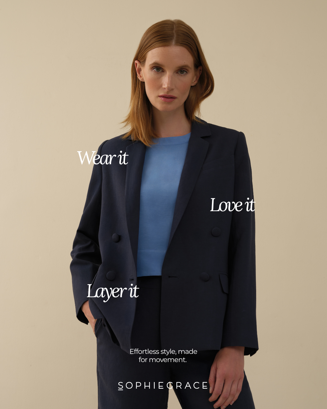 A woman with reddish hair wearing a navy blazer and blue shirt, standing against a beige background, with white text over her saying 'Wear it,' 'Love it,' and 'Layer it.'