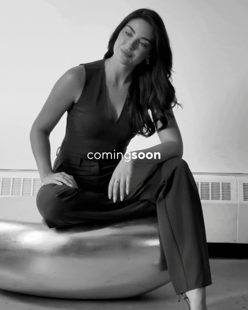 Black and white photo of a woman with long dark hair sitting on a metallic ball, wearing a sleeveless top and wide-leg pants, with the text 'coming soon' overlaid.
