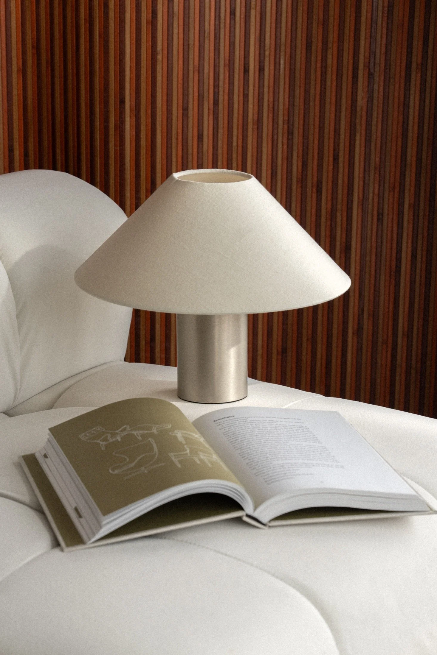 Sculptural table lamp and open art book against a warm wood screen.