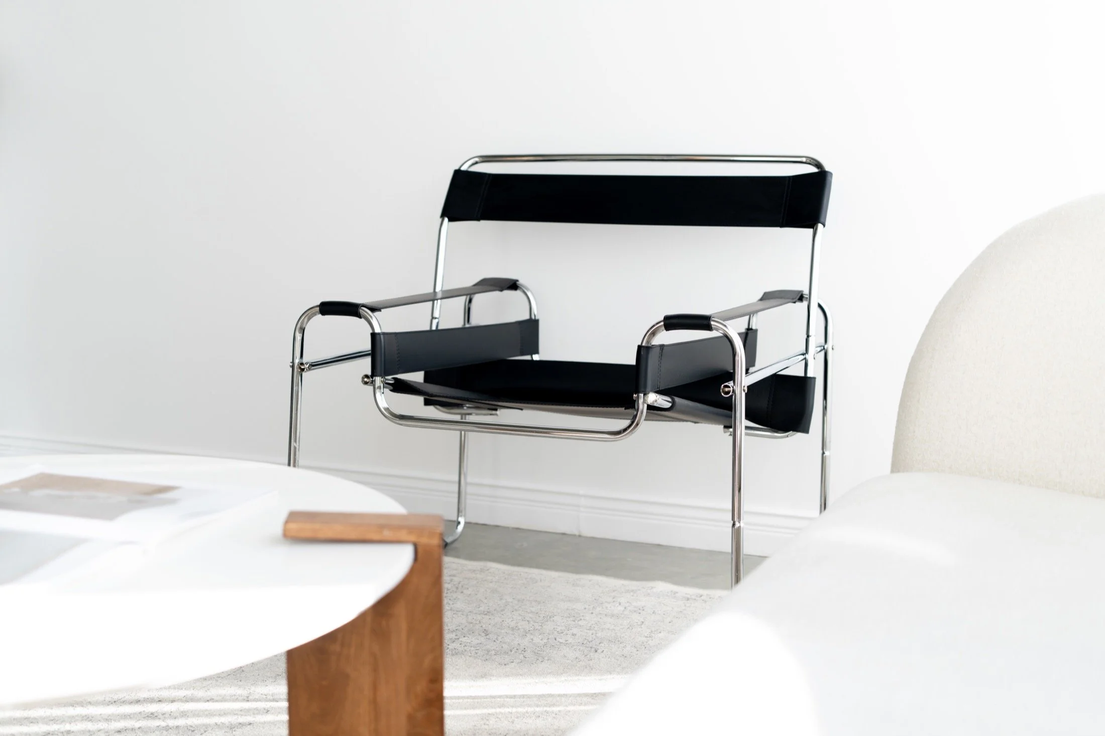 Chrome and black chair framed by cream seating and a round table.