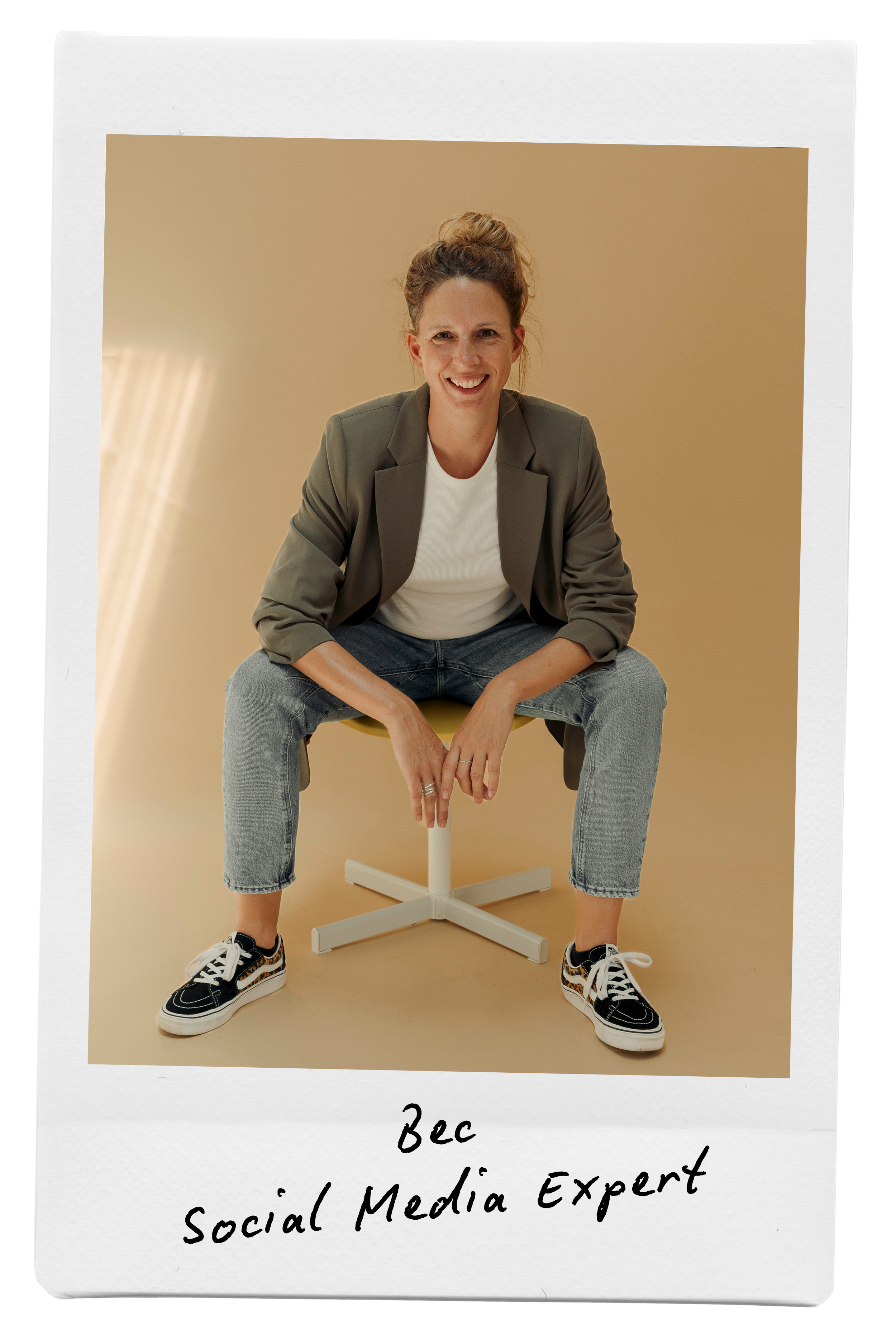 Bec, sitting on a yellow stool, smiling, wearing a gray blazer, white t-shirt, jeans, and sneakers, with handwritten text on the photo that reads 'Bec Social Media Expert'.