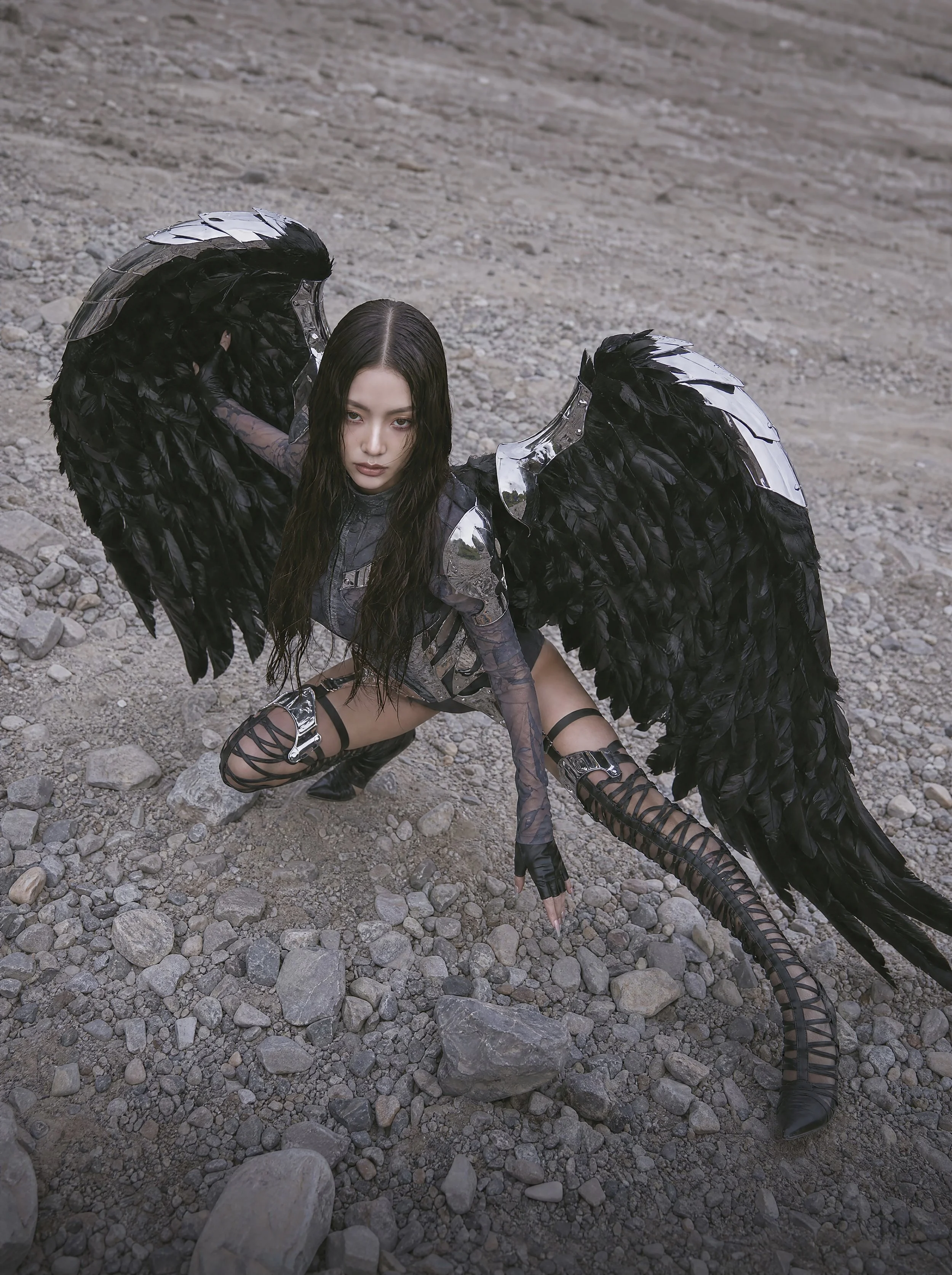 Model Xia Iseri in an otherworldly winged outfit, comprising of chrome and dark fabric, paired with avant-garde laced footwear. The overall vibe of the image exudes an untamed and sovereign energy, inspired by the raven. Outdoor photoshoot.