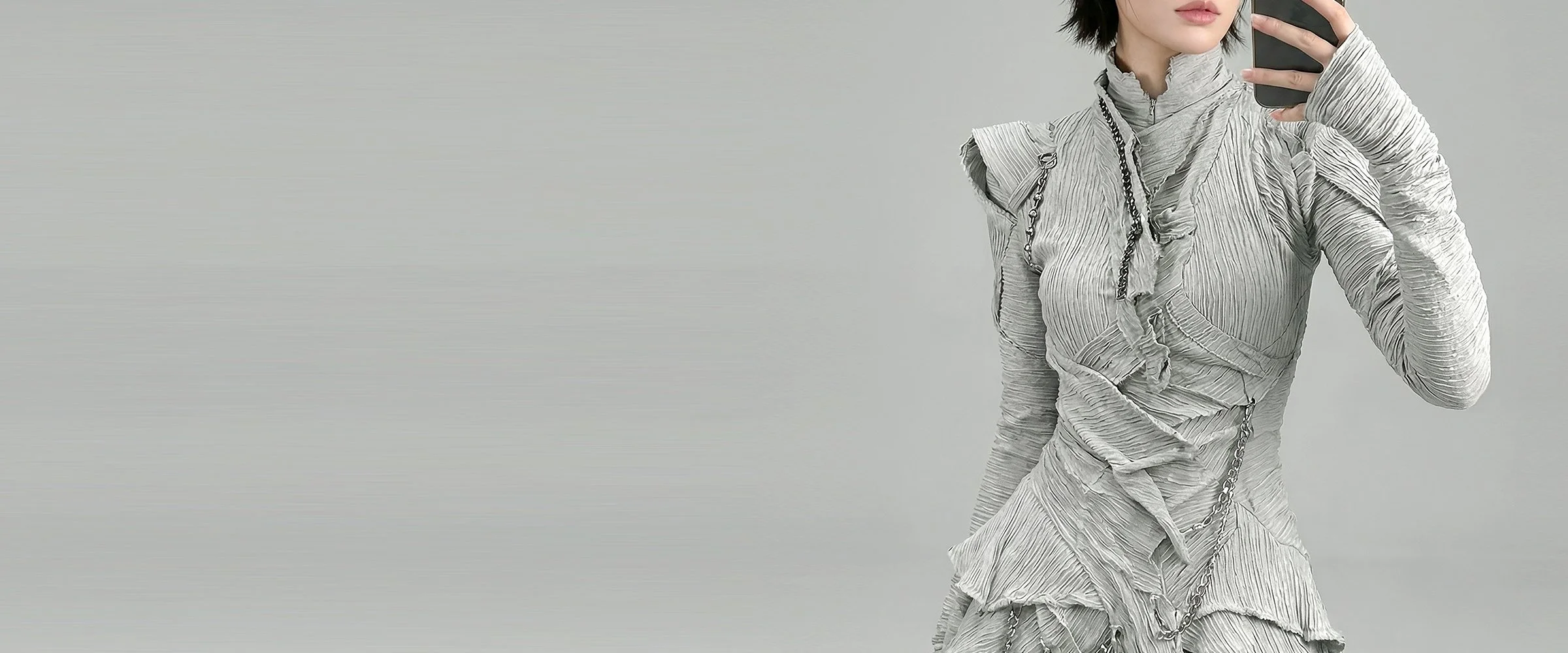 Model and brand ambassador Jun Xeda wearing an otherworldly light gray textured dress that is layered with fitted bodice, expressed ruffles and a draped hemline. She is wearing thigh high silver boots with a tabi toe design, for digital fashion brand