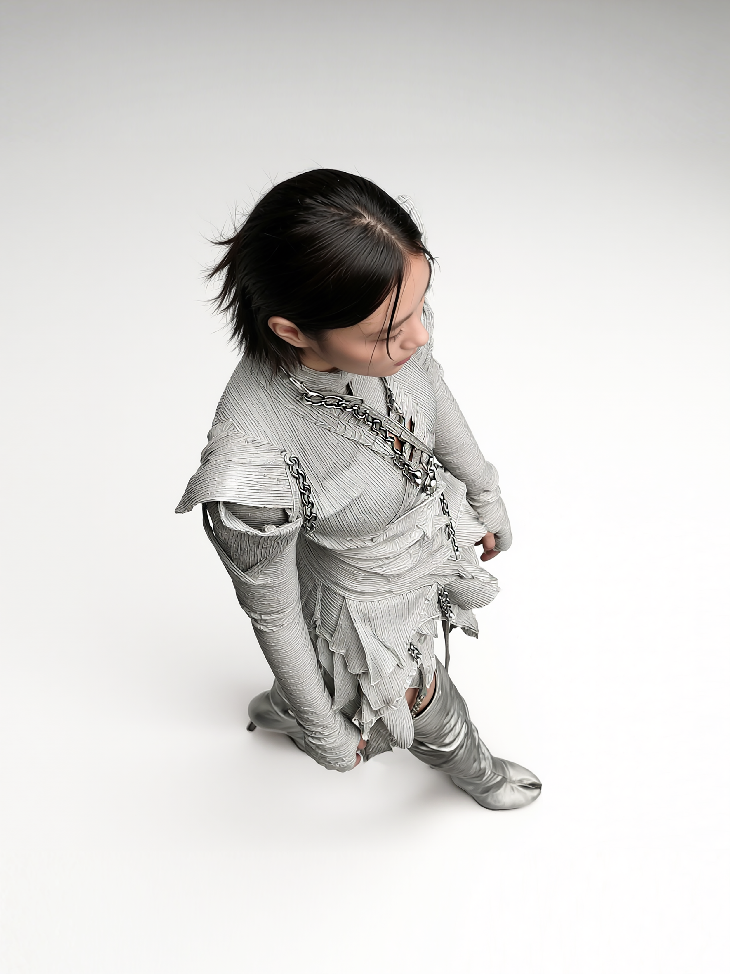 Model and brand ambassador Jun Xeda wearing an otherworldly textured dress that is layered with fitted bodice, expressed ruffles and a draped hemline. She is wearing thigh high silver boots with a tabi design, for digital fashion brand [ze Luna].