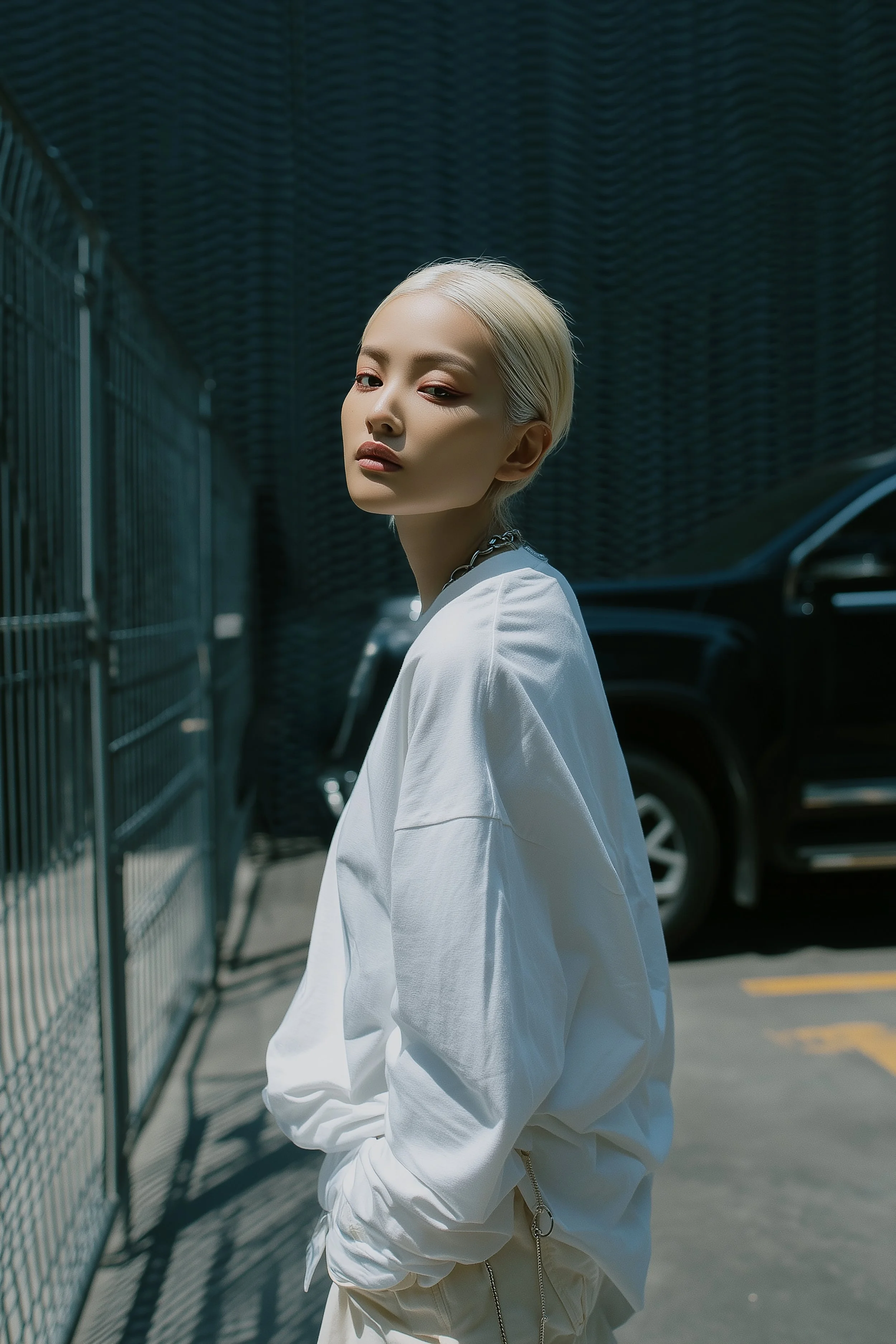 Model Xia Iseri posing in a casual white shirt and pants, staring at the camera. The scene is in a parking lot somewhere on Earth. She looks relaxed and casual, yet her stare is deep and intense.