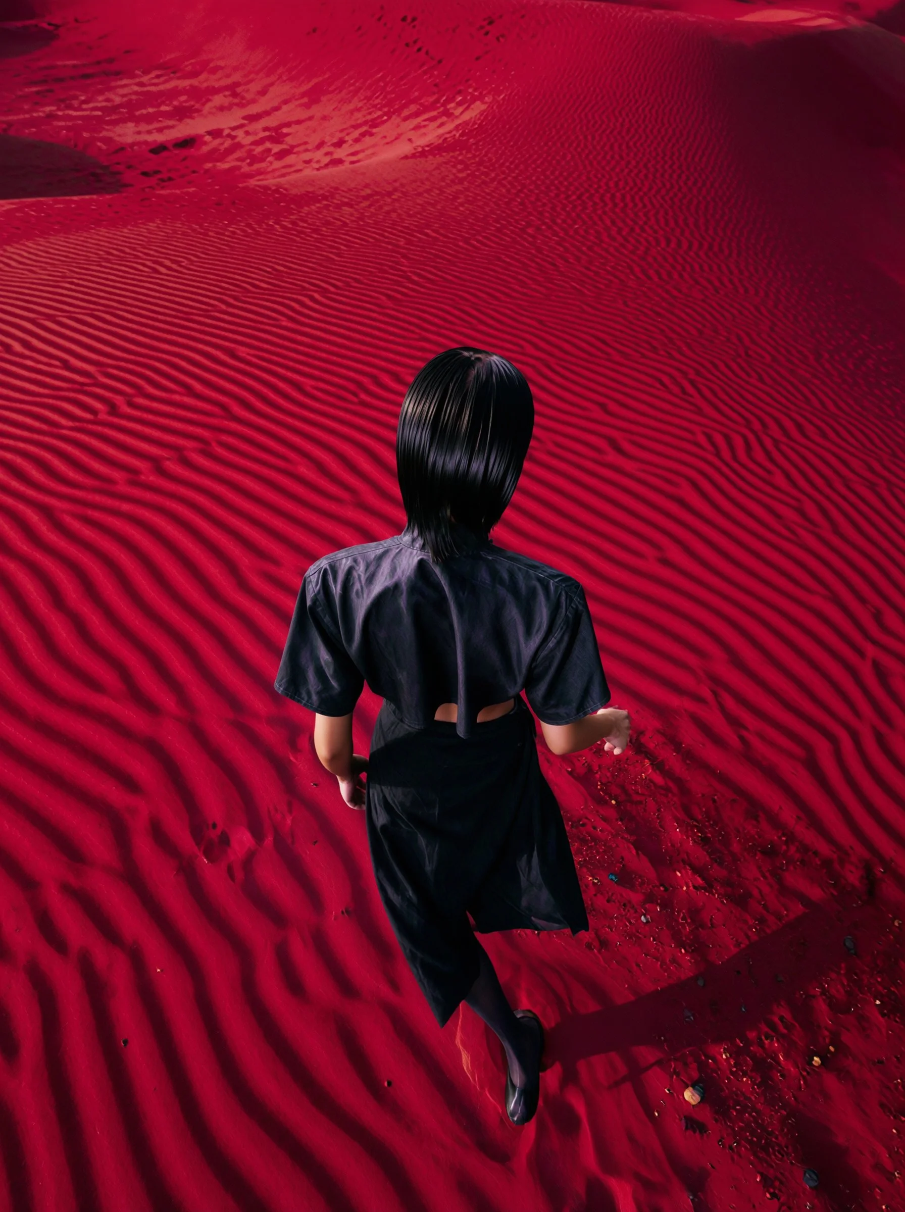 Model Xia Iseri posing in a new-age Chinese Qipao in a deep-red sandy desert like environment. The outfit consists of a cropped top, matching skirt and black stockings, complete with oriental details that fuses modernity with tradition.