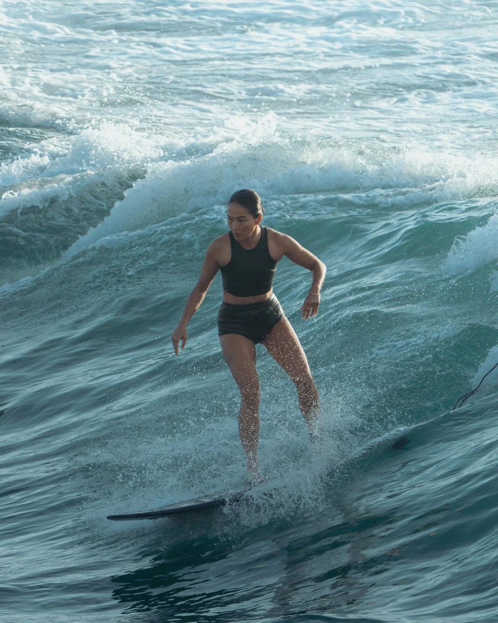 A woman in black sportswear riding a surfboard on ocean waves.