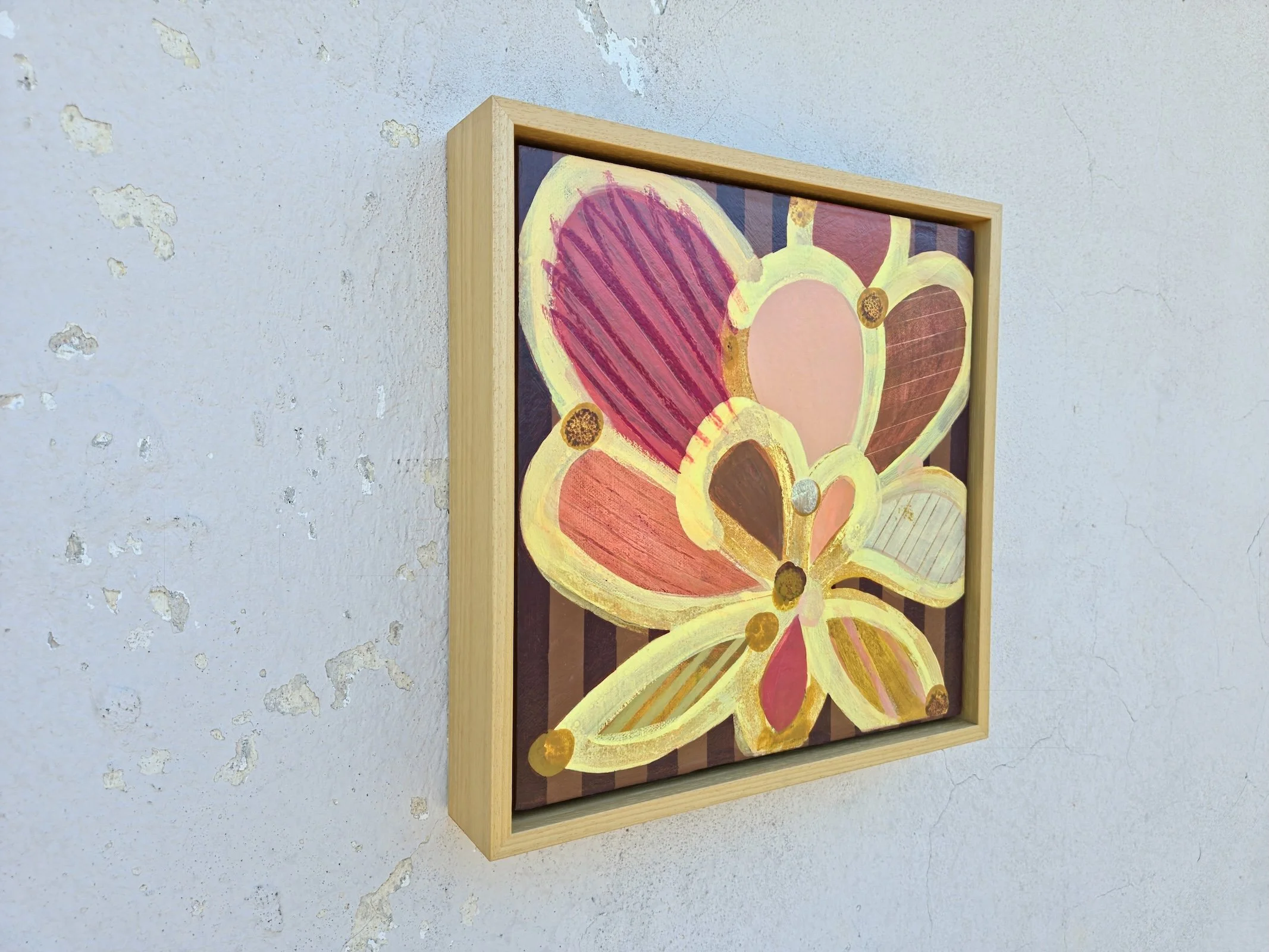 framed botanical painting in yellows and pinks on a striped background, angled view