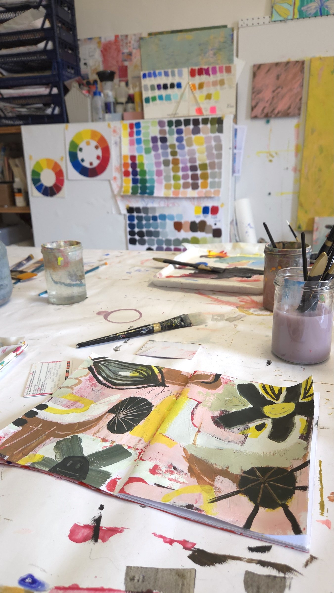 open sketchbook on a table with art supplies and colour wheel on the wall