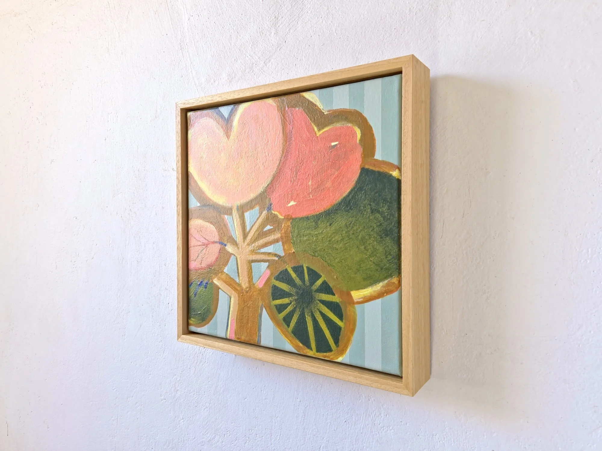 framed botanical painting in bright pinks and greens on a striped background, angled view