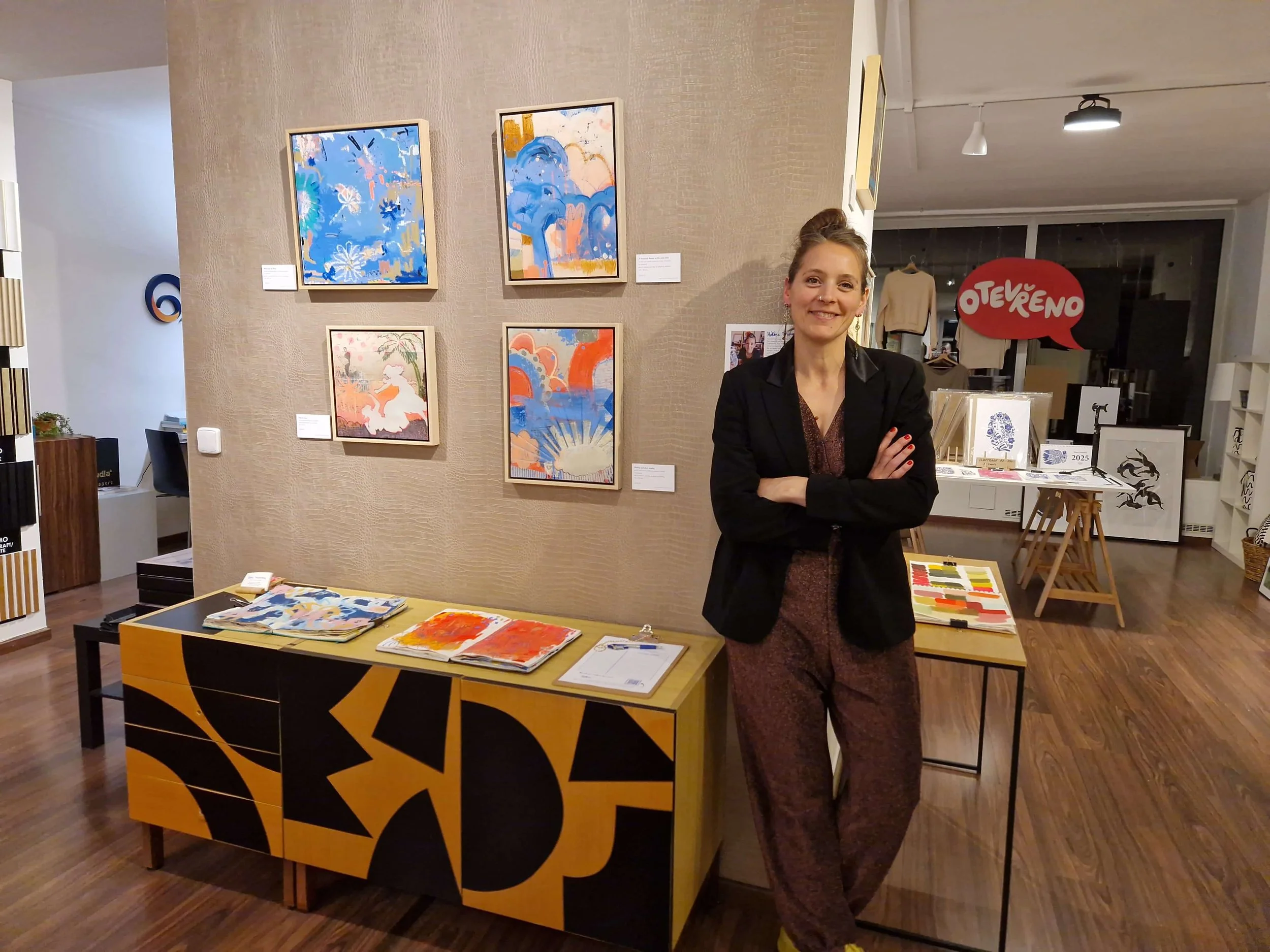 woman artist standing proudly in front of her paintings hanged in a gallery