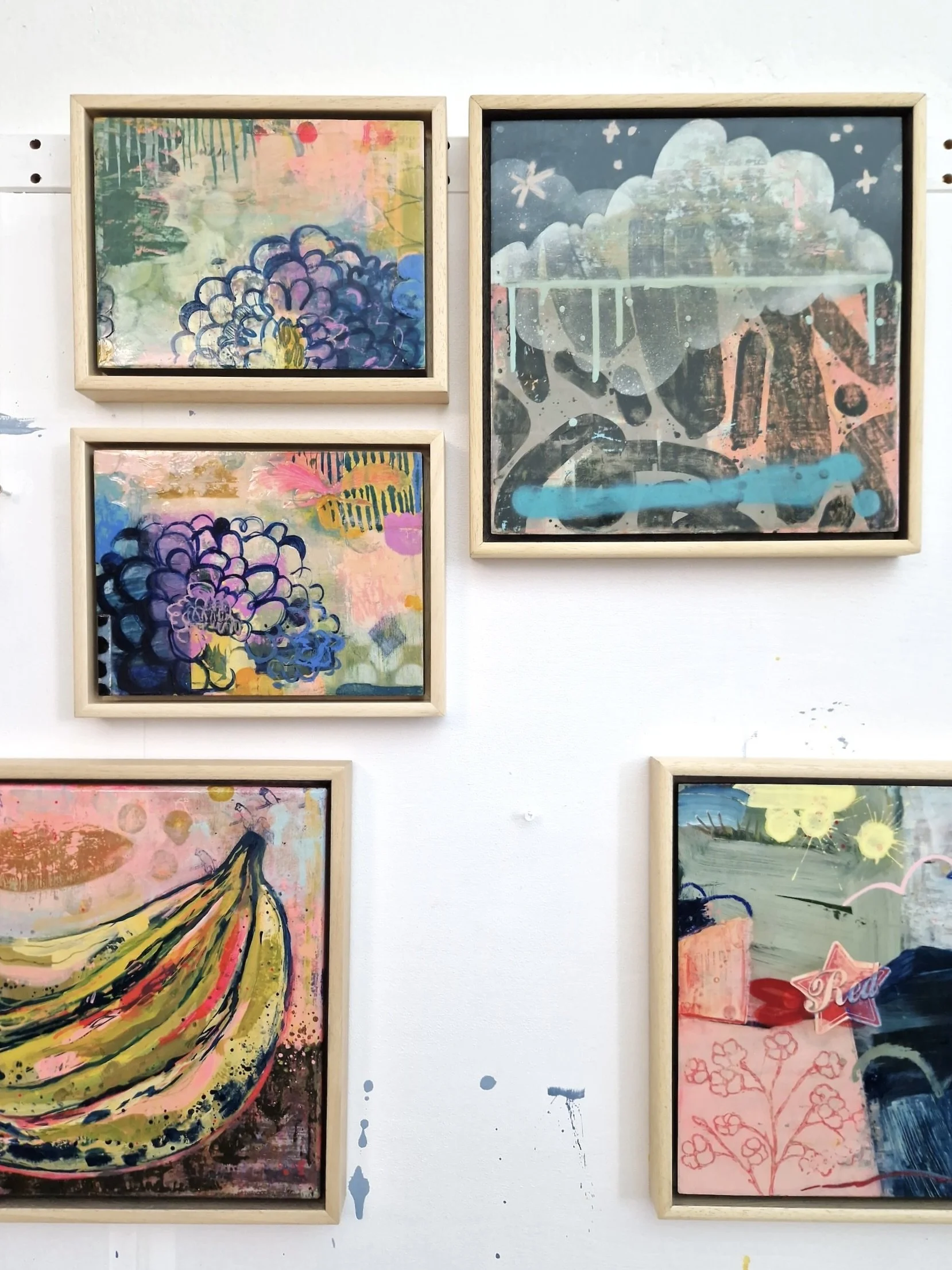 Collection of five colorful, abstract paintings framed in light wood displayed on a white wall.