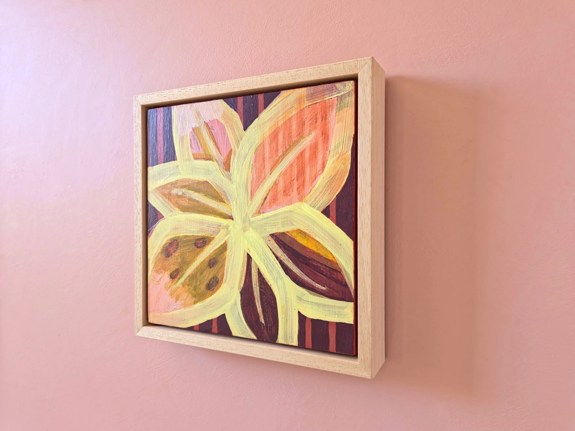 angled view of a framed botanical painting in pinks, yellows and browns