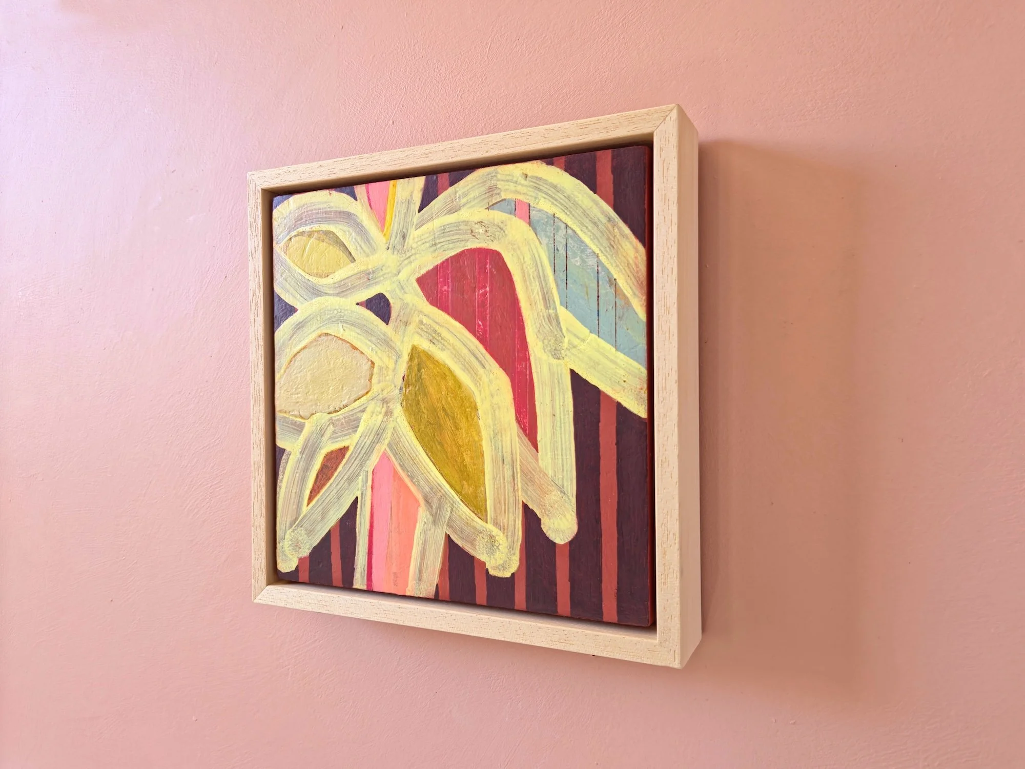 framed botanical painting in vibrant colours with a striped background on a pink wall