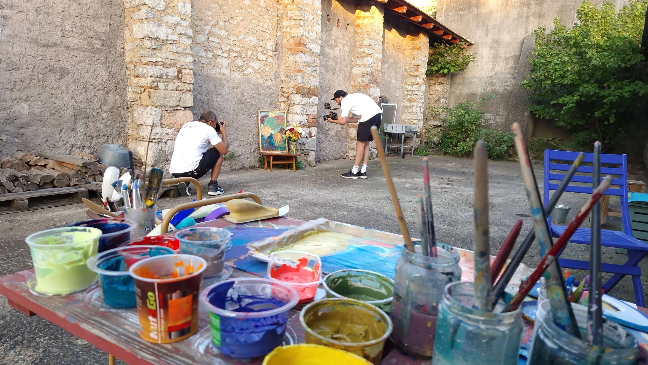 Outdoor artist setup and photographers in action around a finished botanical painting