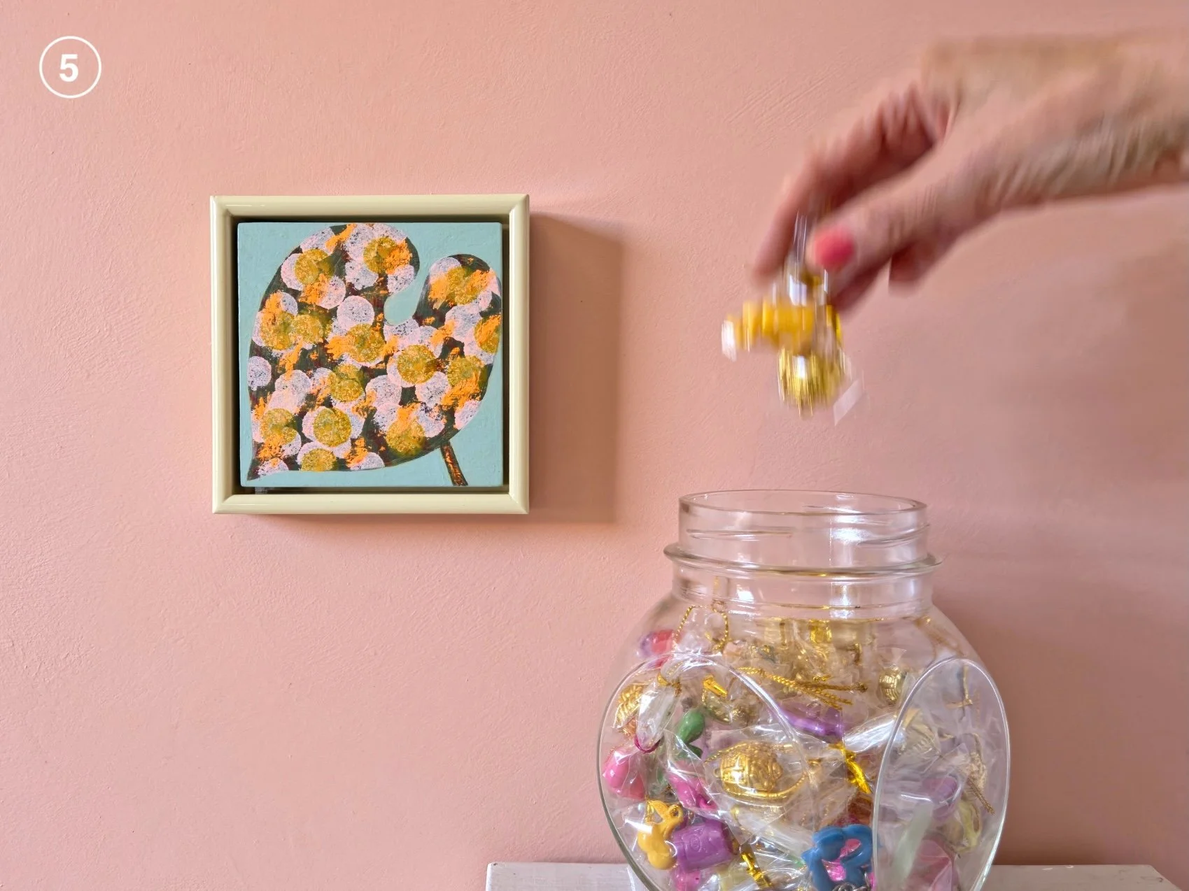 small framed botanical painting on a pink wall next to jar of candies