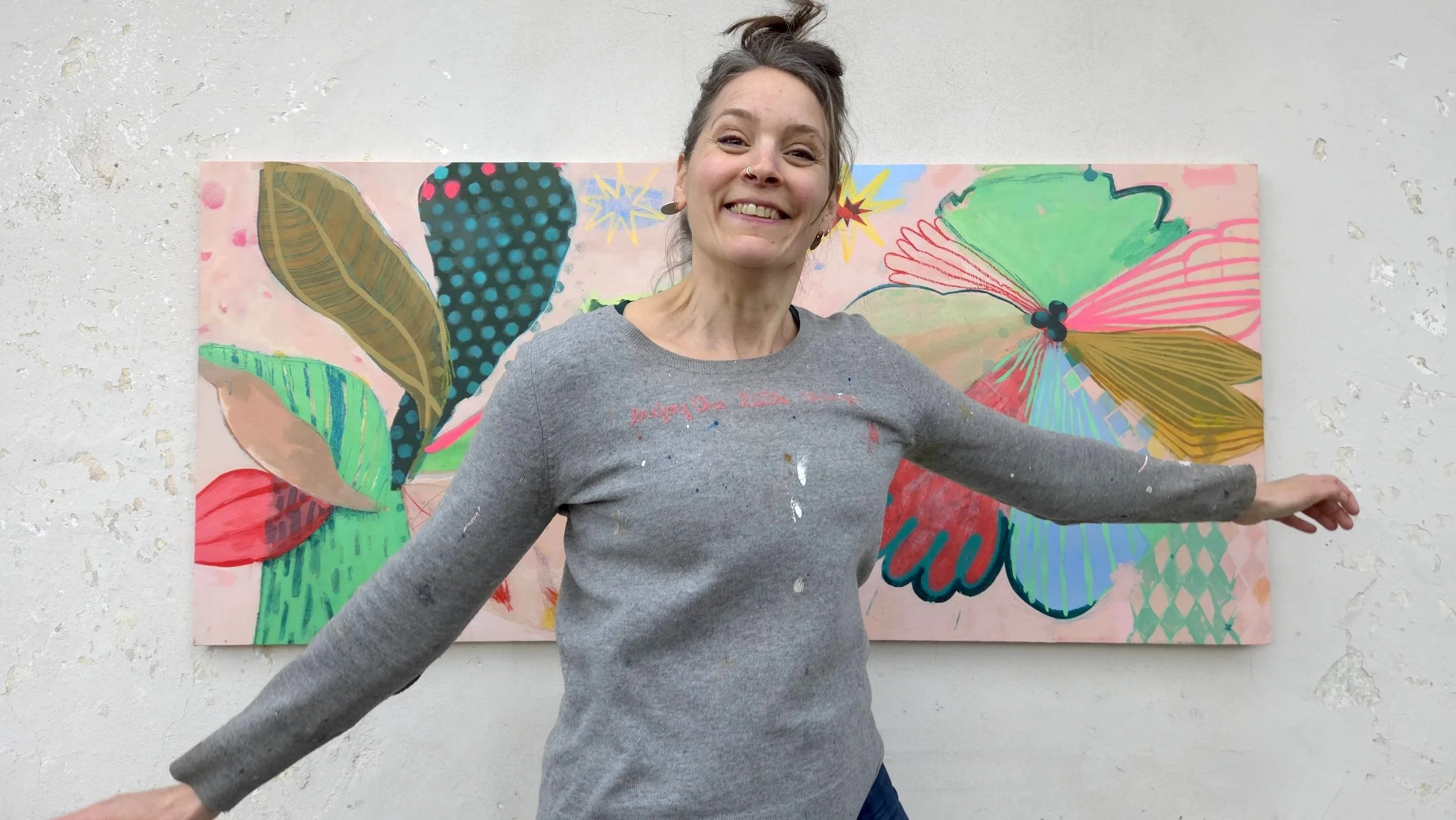 woman artist jumping in front of a wall where are hanged two colourful palm tree paintings