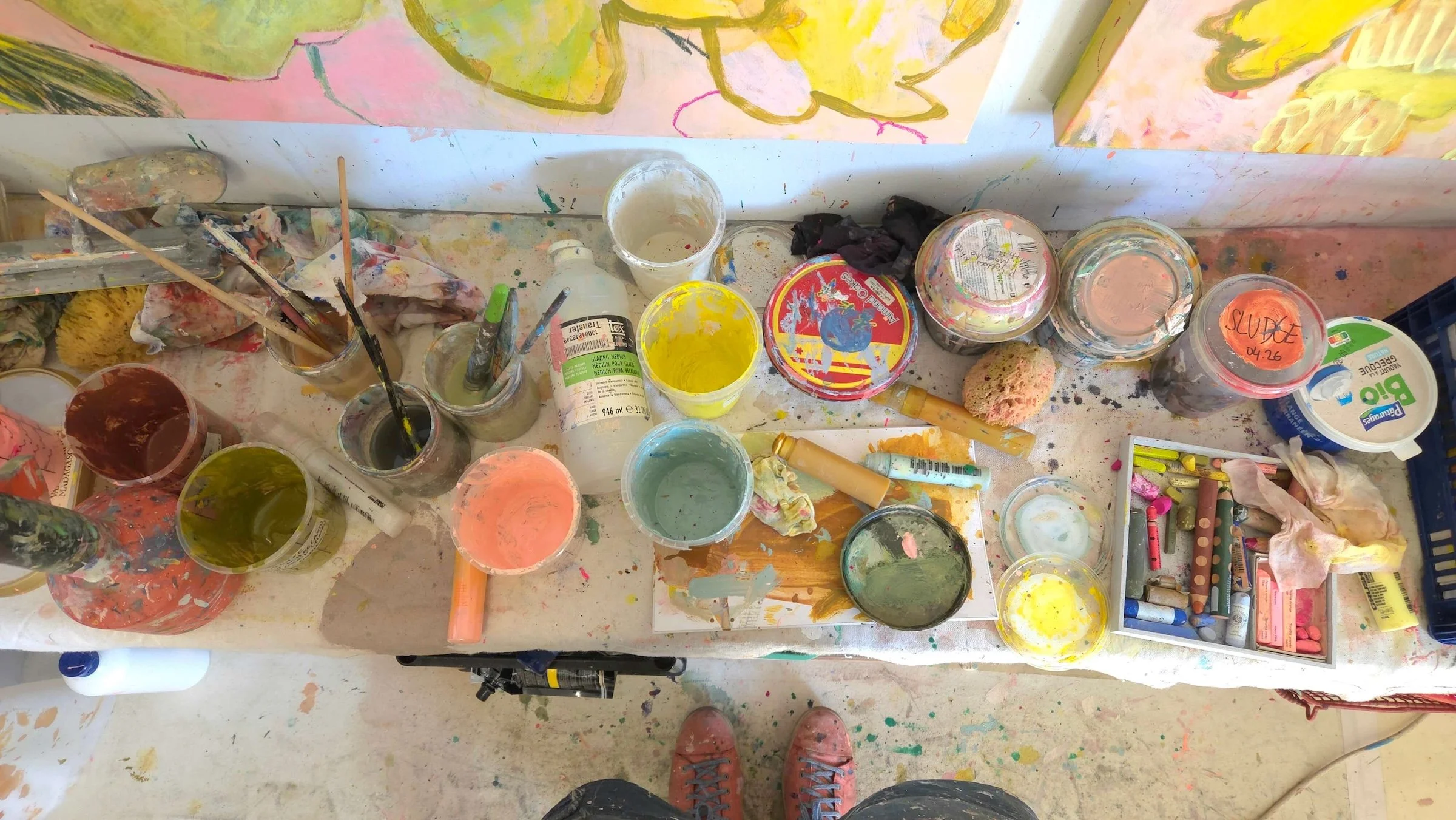 paint posts and brushes and crayons on a bench under two canvases habnged on a wall