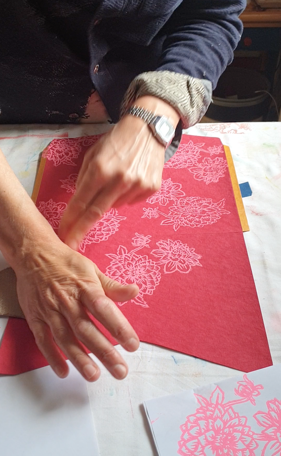 hands a t work, printing a pink flower pattern with lino onto a red pocket