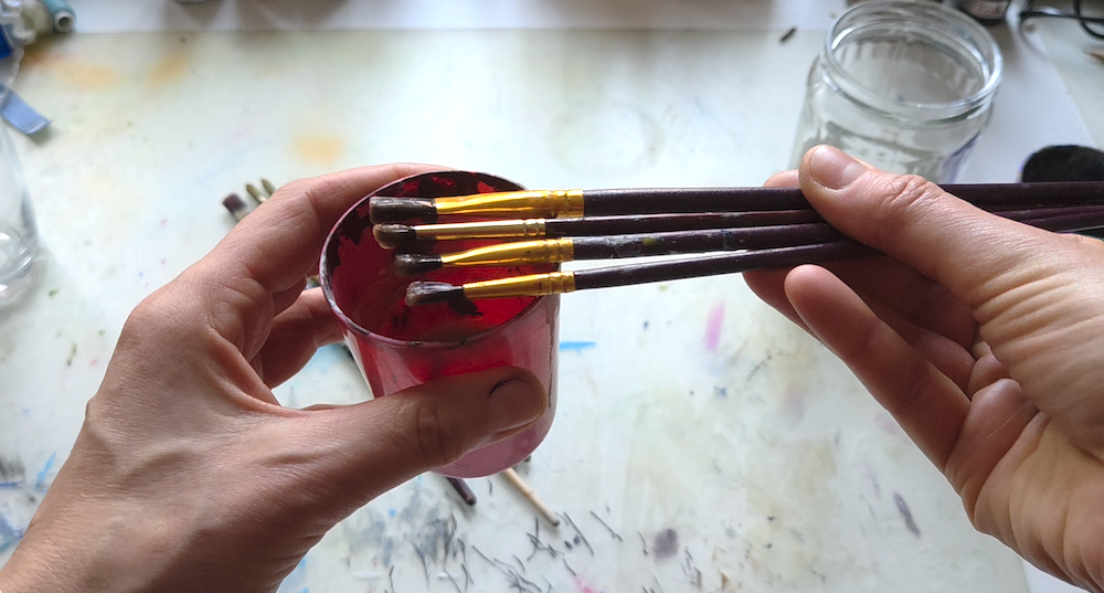 artist's hands showing a bunch of brushes covered in hydroalcoholic gel, cleaned from dry acrylic paint