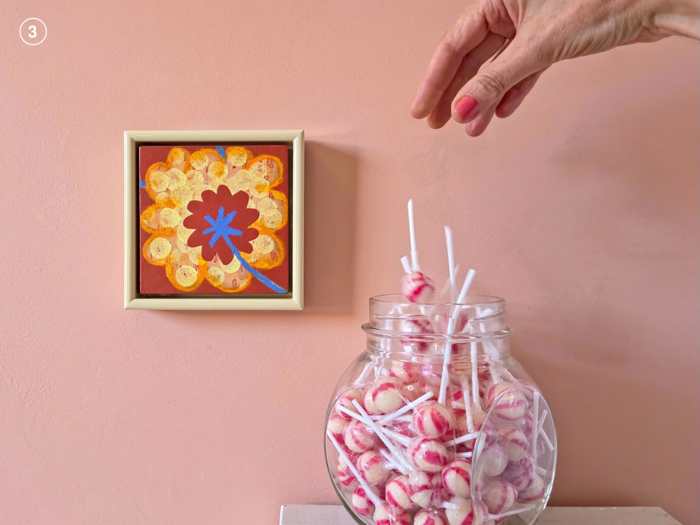 small framed botanical painting on a pink wall next to jar of candies
