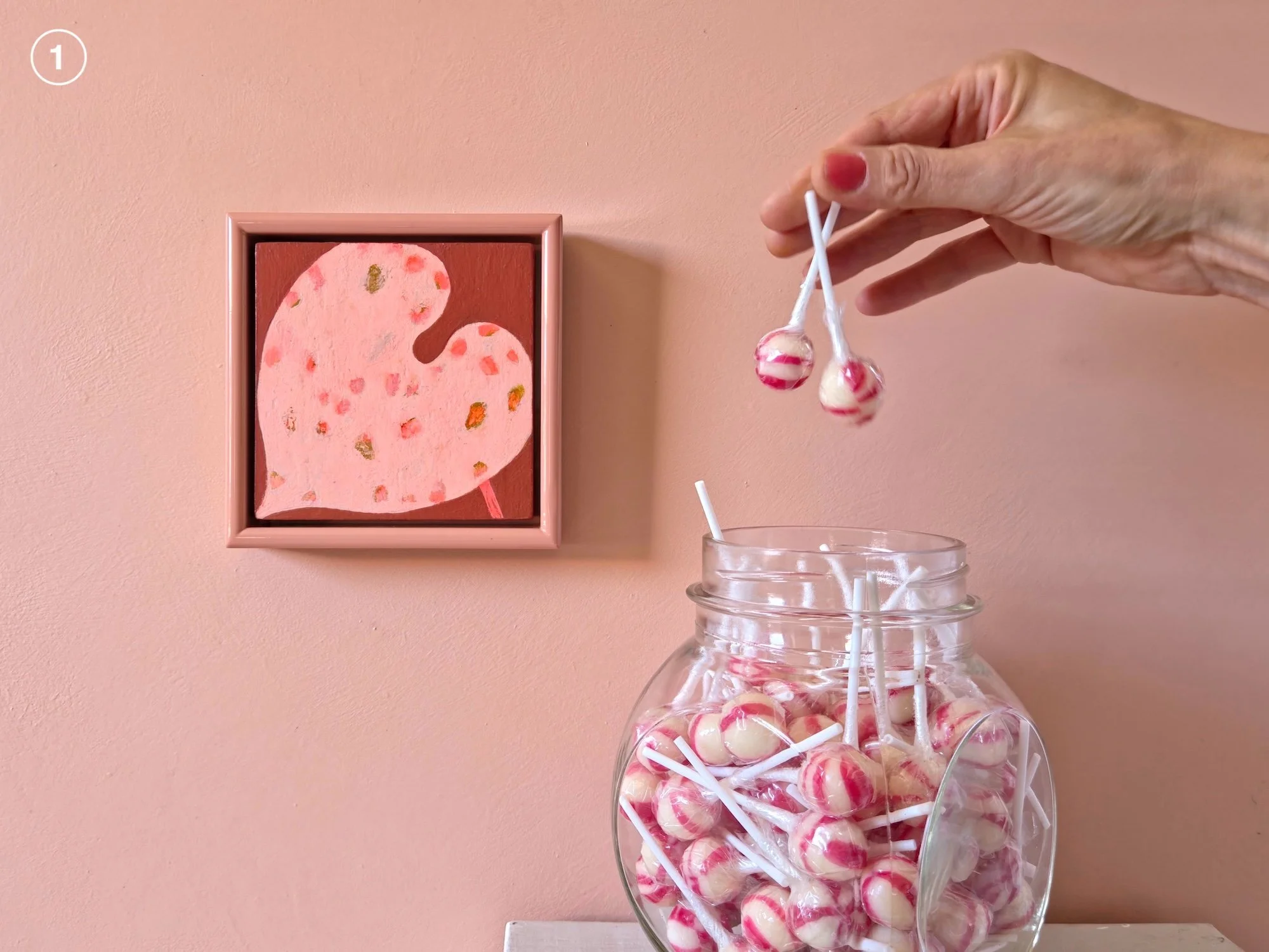 small framed botanical painting on a pink wall next to jar of candies