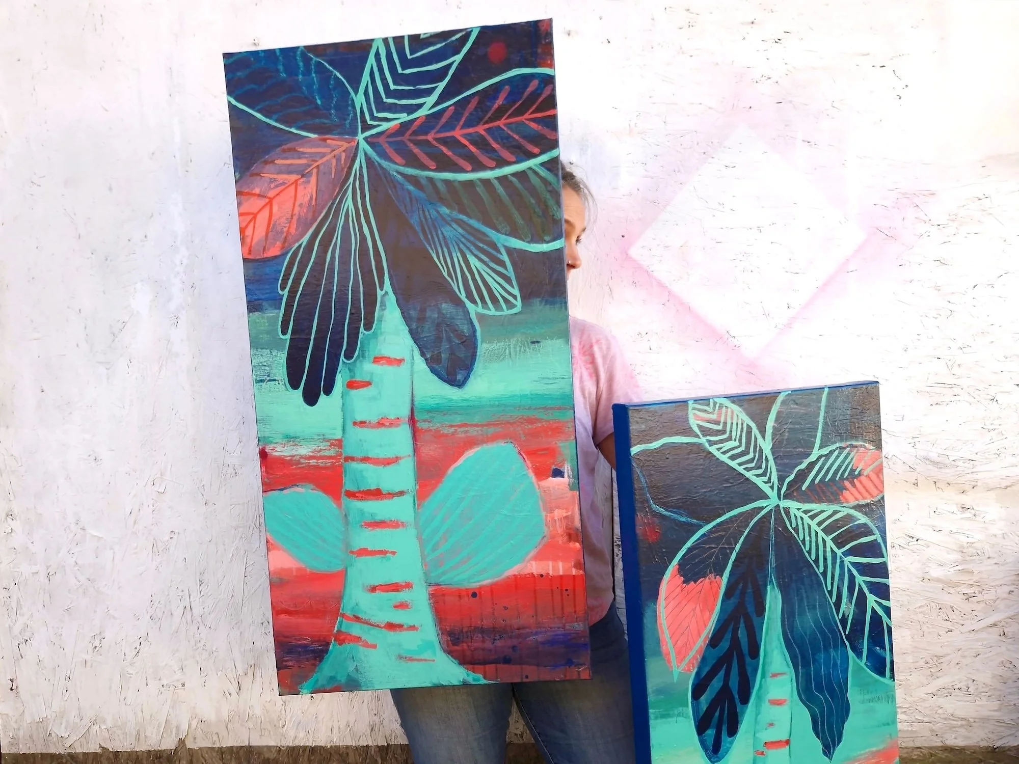 Artist holding two abstract mixed media canvases in the studio, layered textures and botanical inspired shapes.