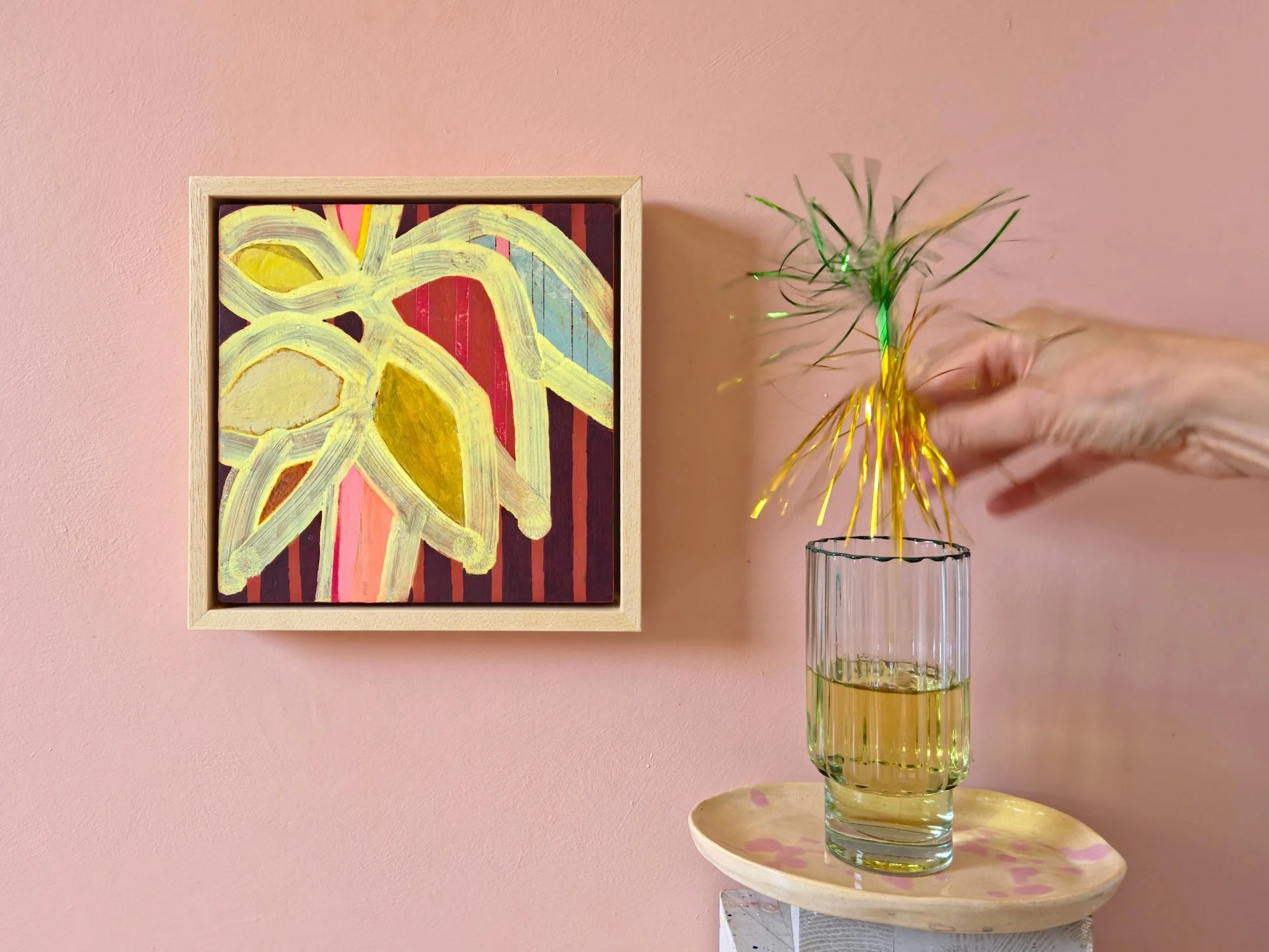 framed botanical painting in vibrant colours with a striped background on a pink wall next to a cocktail glass