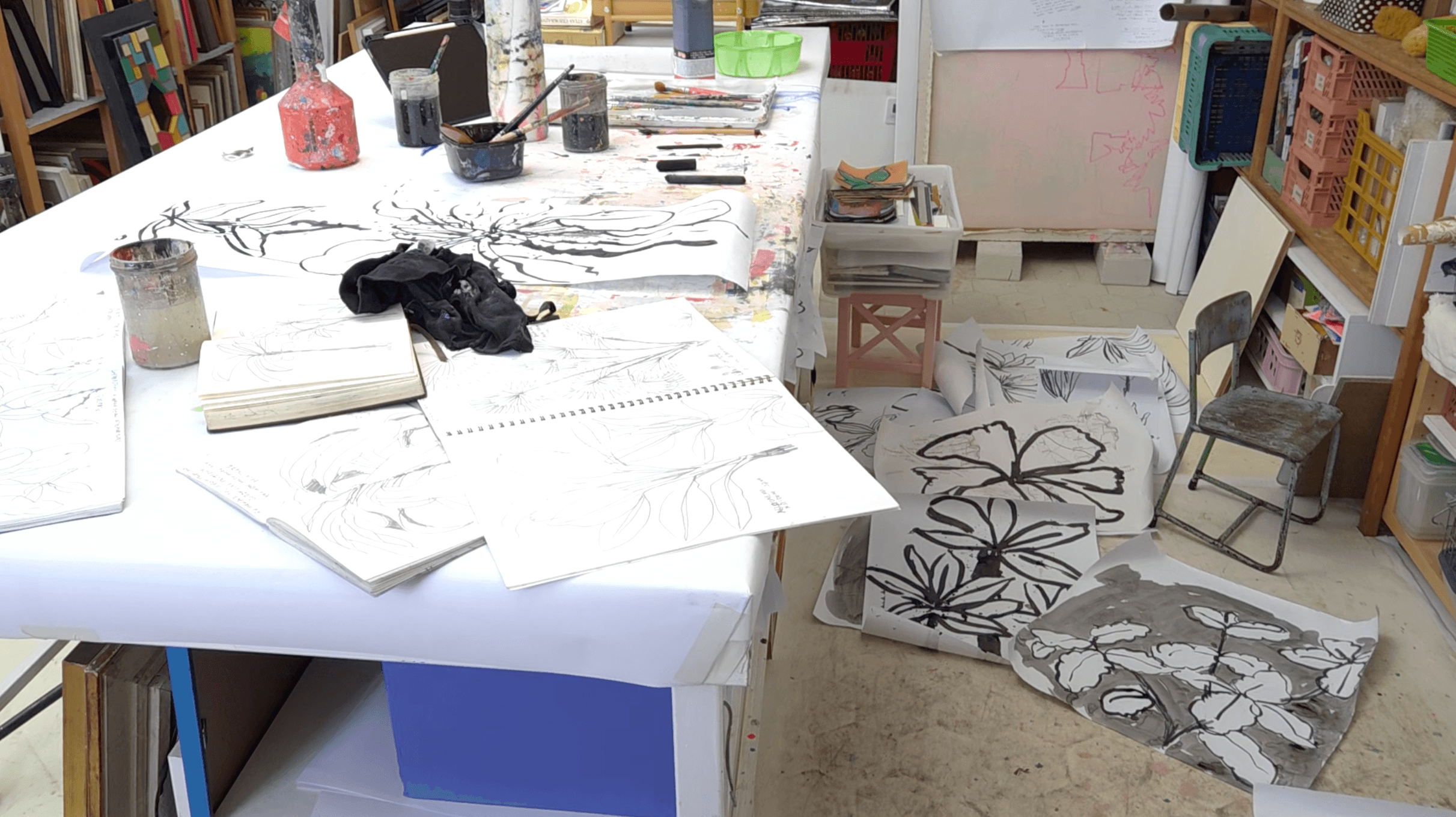 Messy art studio table and floor after a painting session with papers, paints, brushes and tools scattered.
