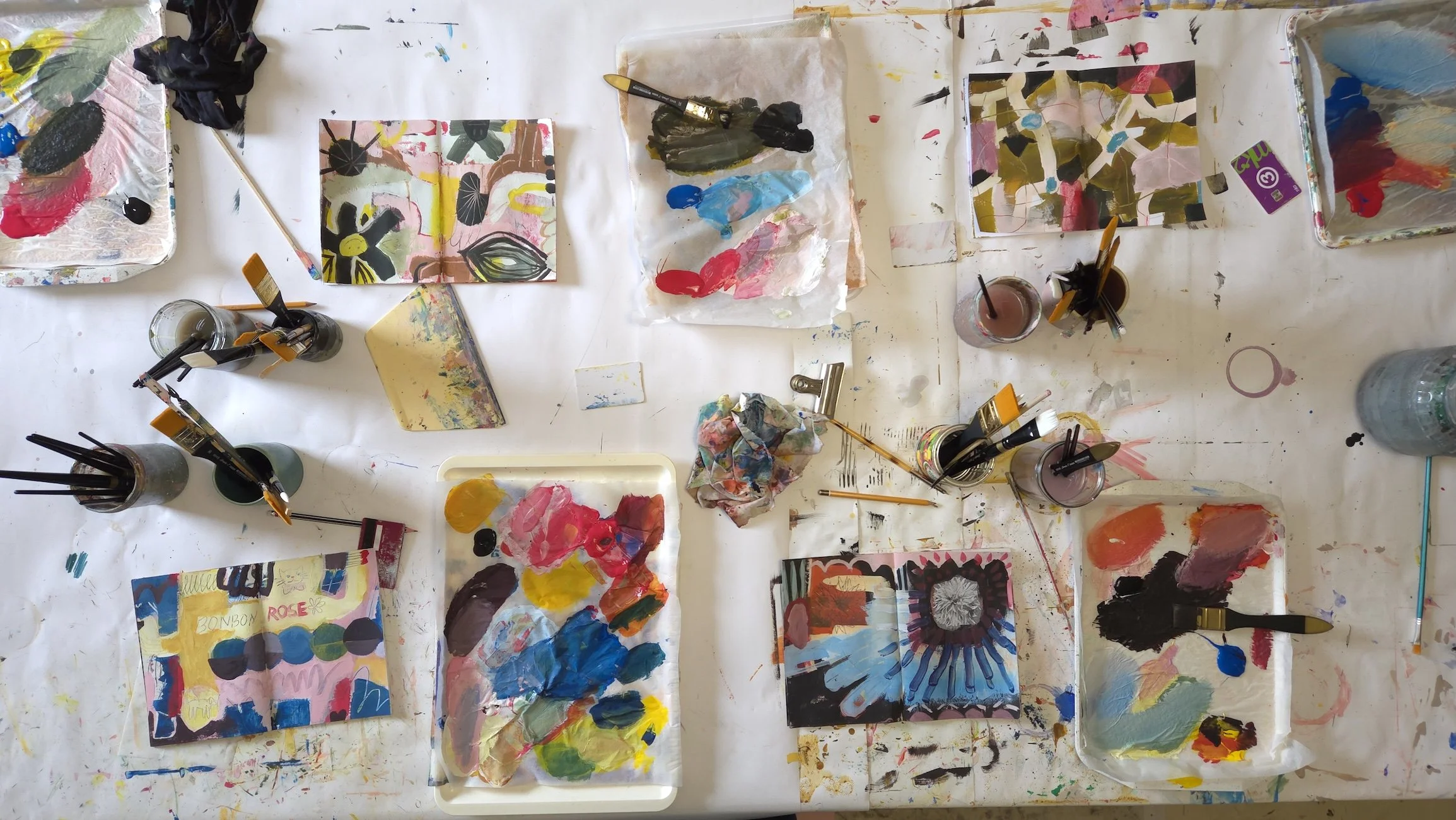 top view of a table with open sketchbooks, painting palettes, brushes and other art supplies