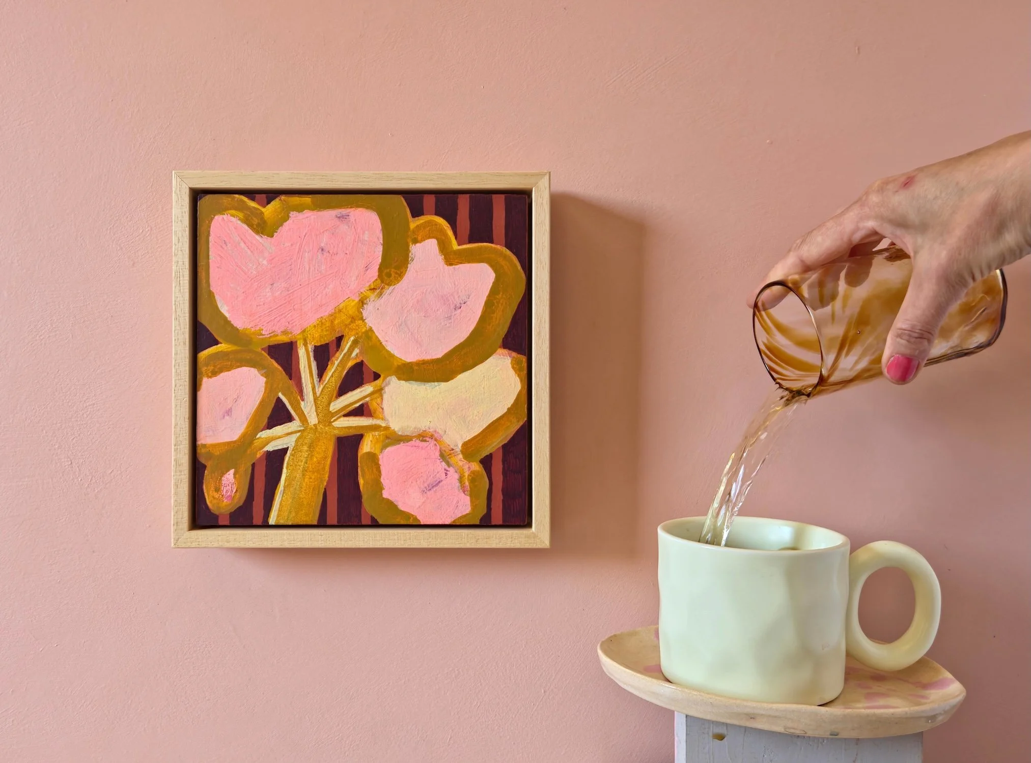 framed botanical painting in pinks and browns on a pink wall next to a cup of tea